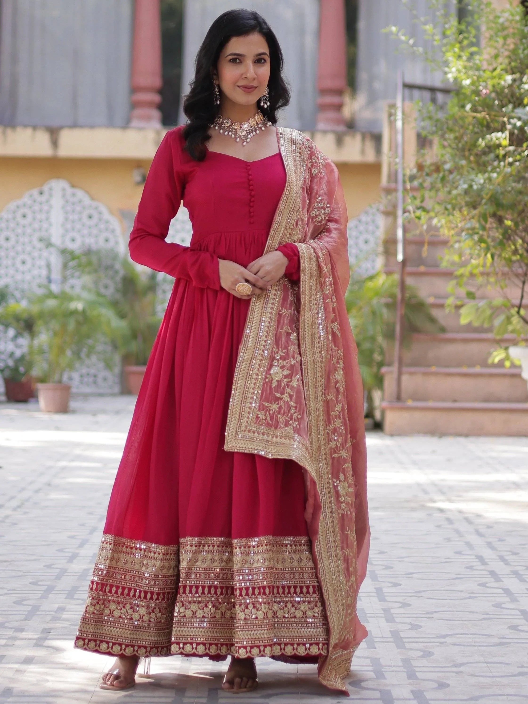 Woman in a red border work ethnic gown with gold embroidered dupatta, outdoor setting