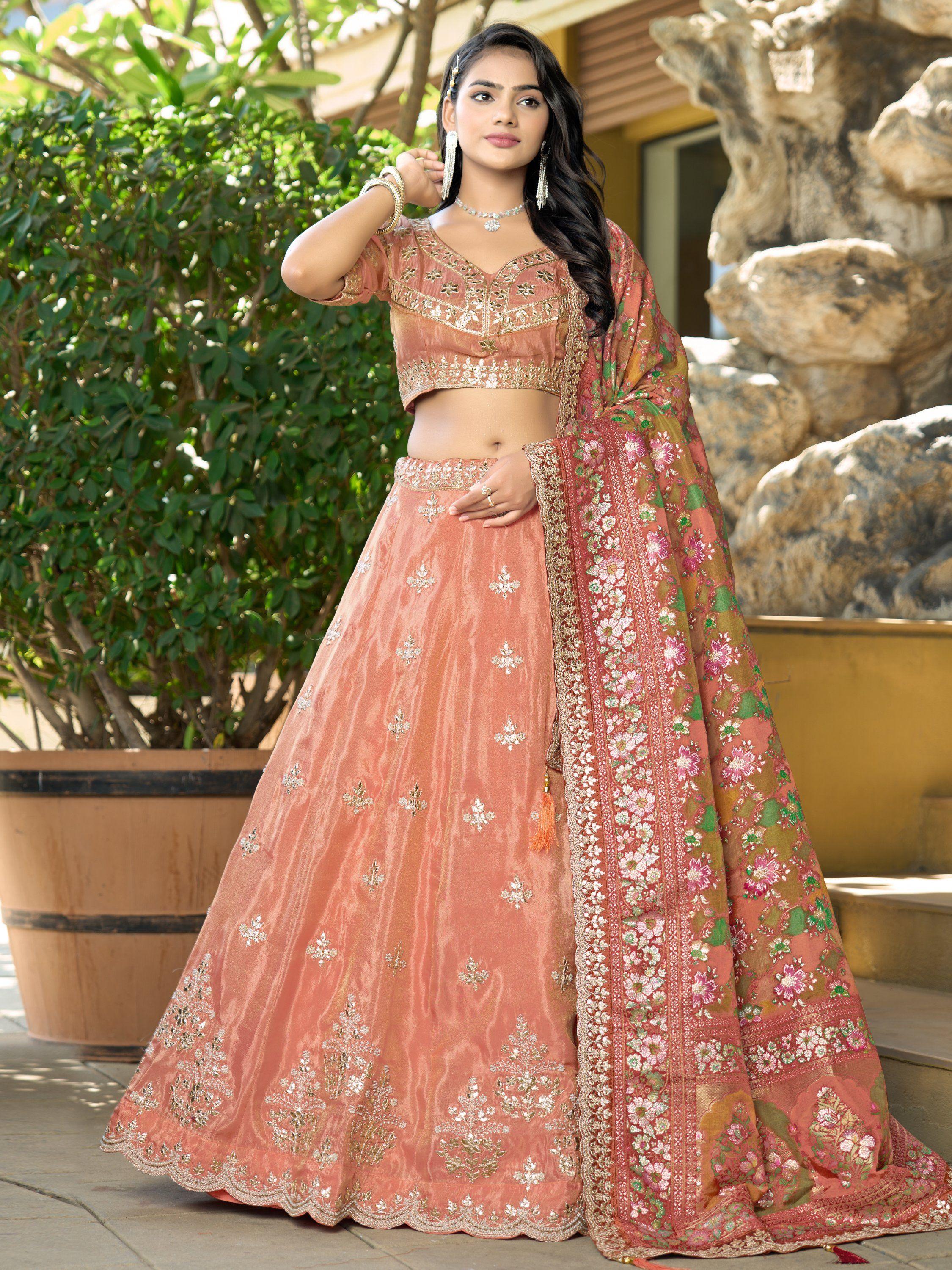 Woman wearing orange bridal lehenga choli with gold embroidery and floral dupatta outdoors