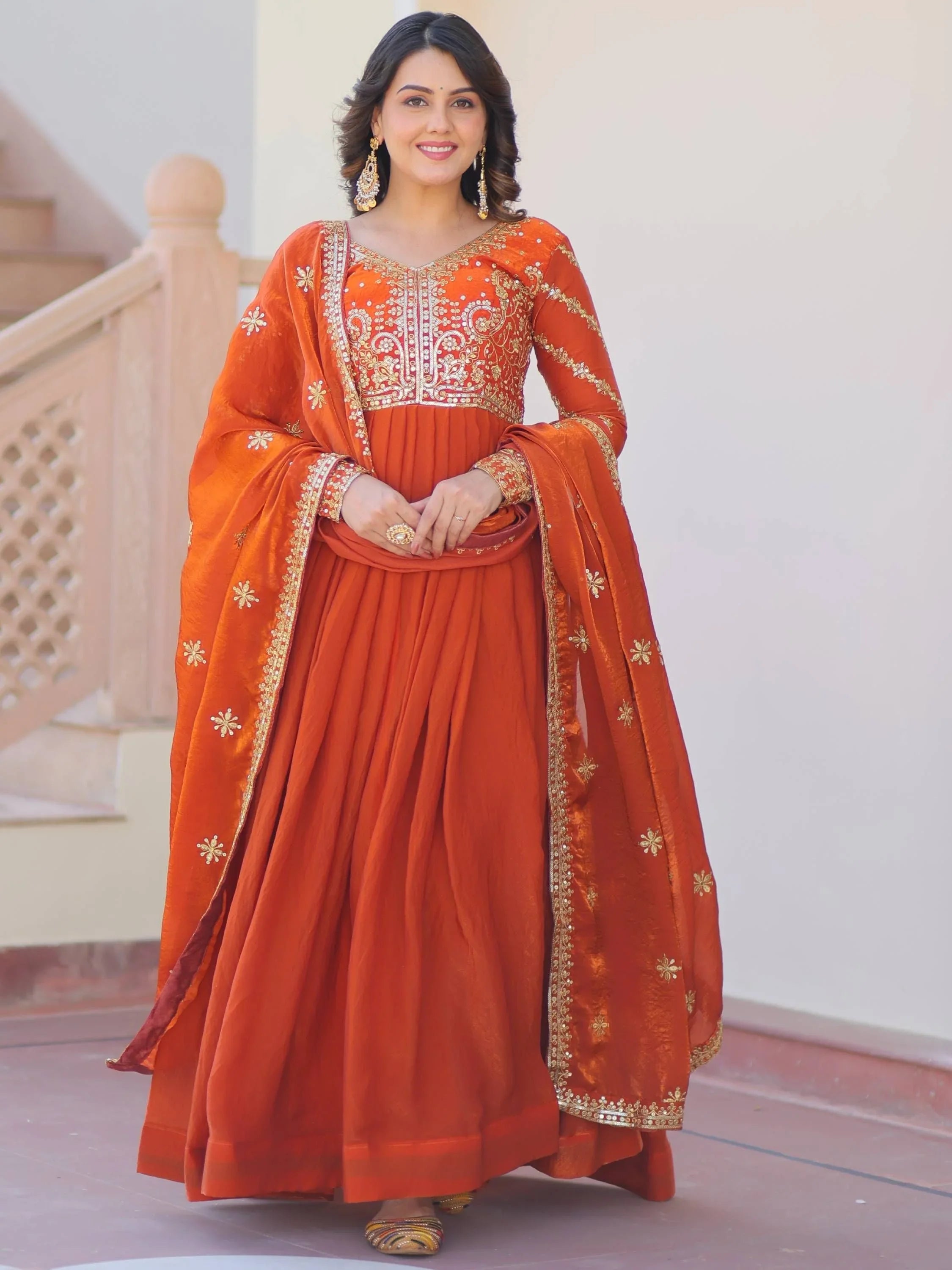 Woman wearing orange embroidered engagement gown with gold dupatta and traditional jewelry