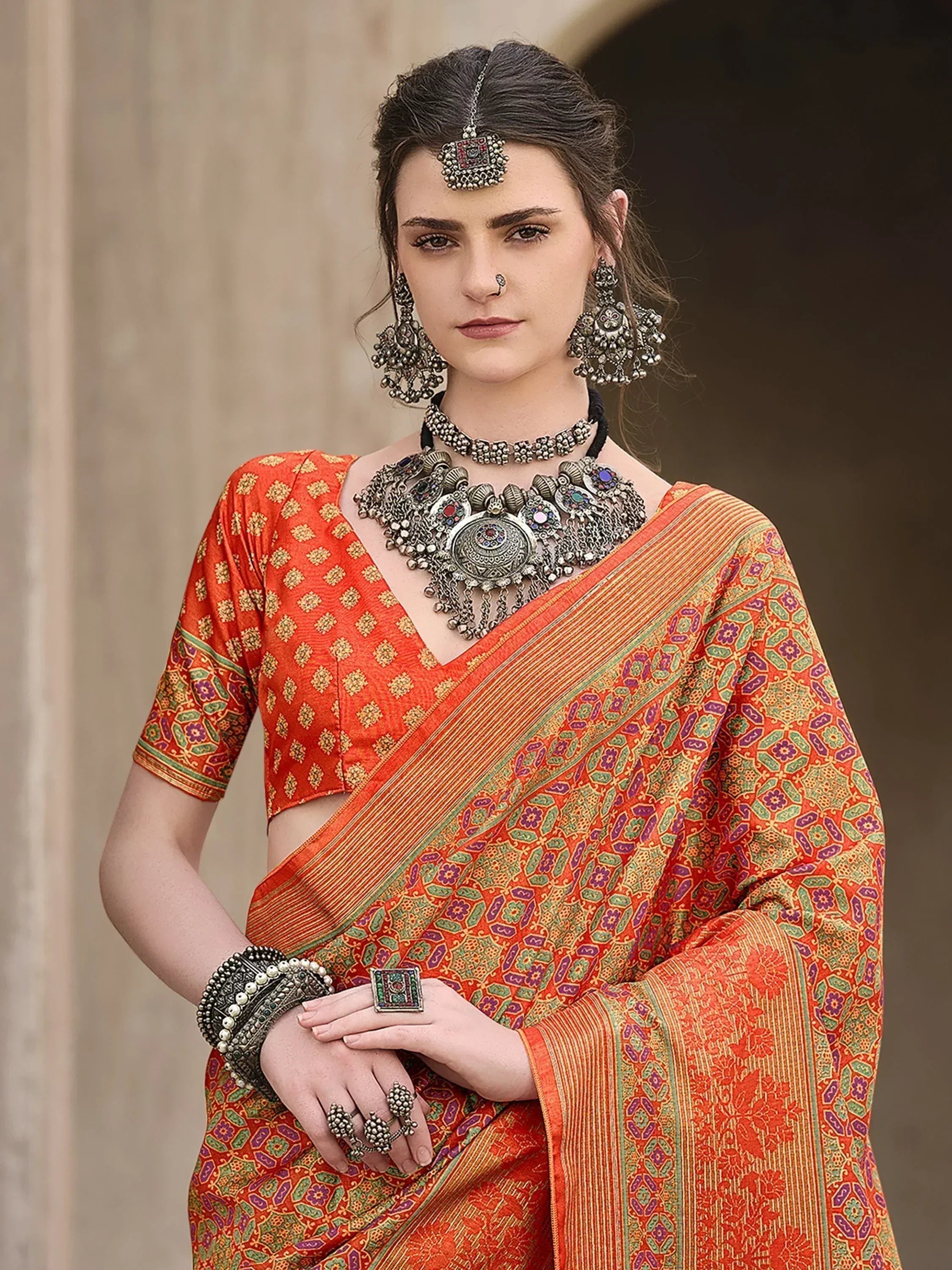 Woman in vibrant orange printed saree with ethnic jewelry, perfect for Indian festive occasions.