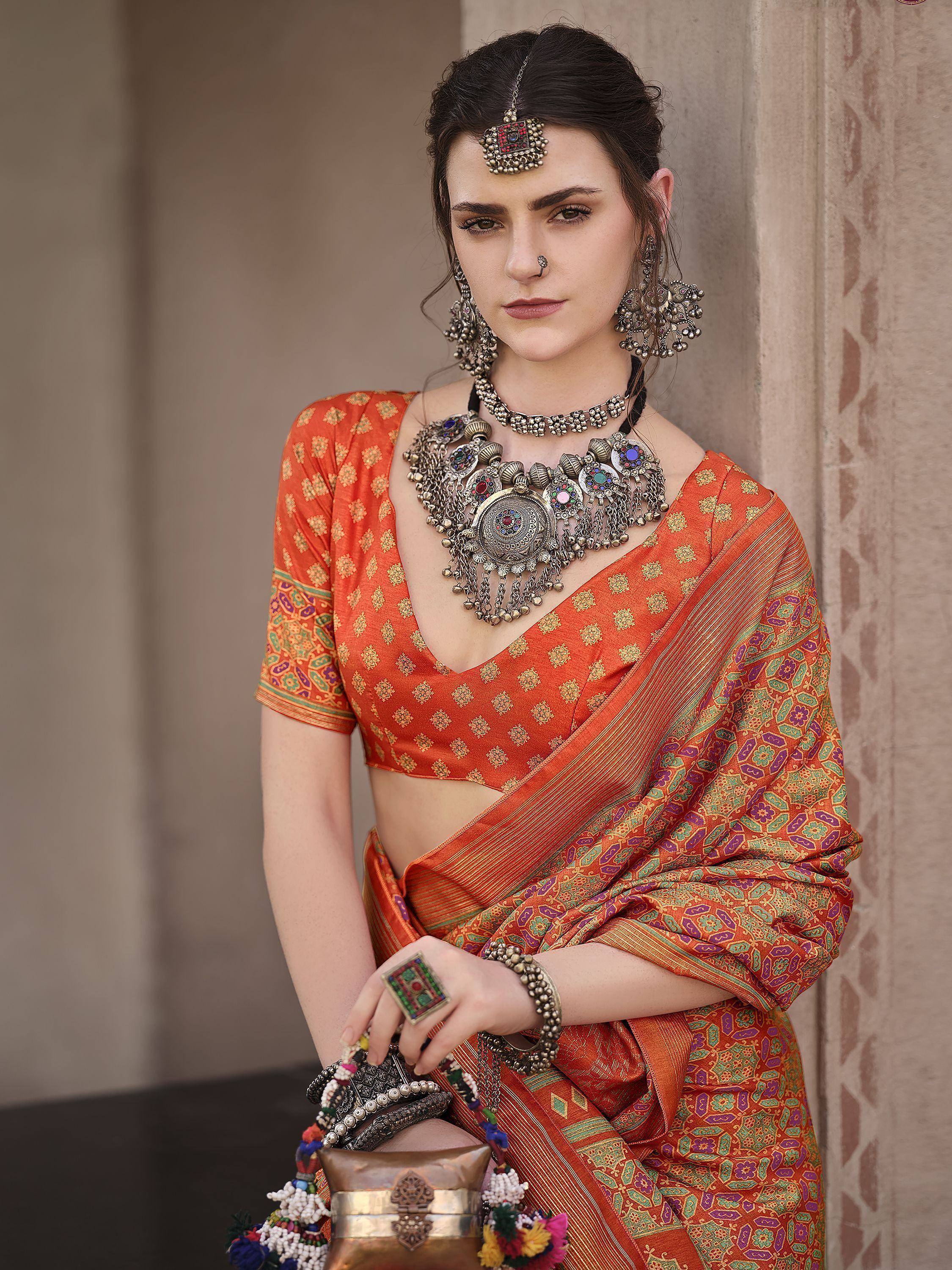 Woman in vibrant orange printed saree with heavy ethnic jewelry, showcasing traditional Indian ethnic wear.