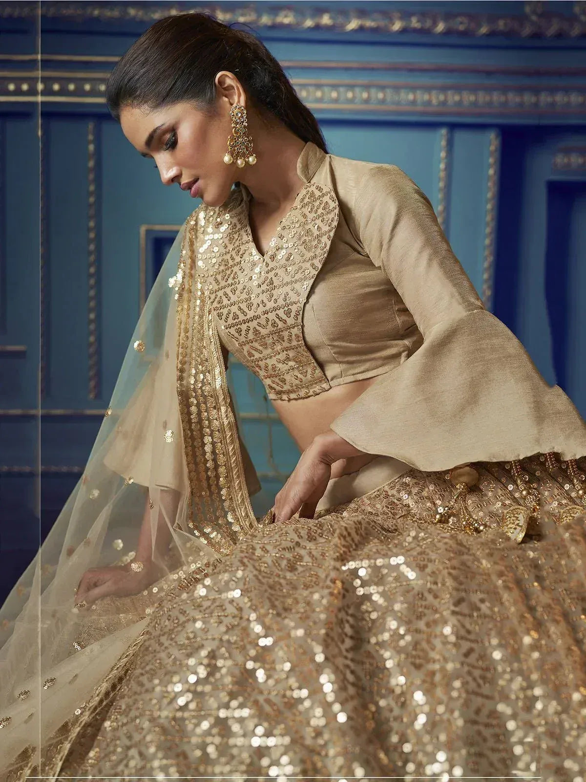 Elegant gold sequin lehenga choli with bell sleeves and sheer dupatta, perfect for Indian ethnic wear occasions.