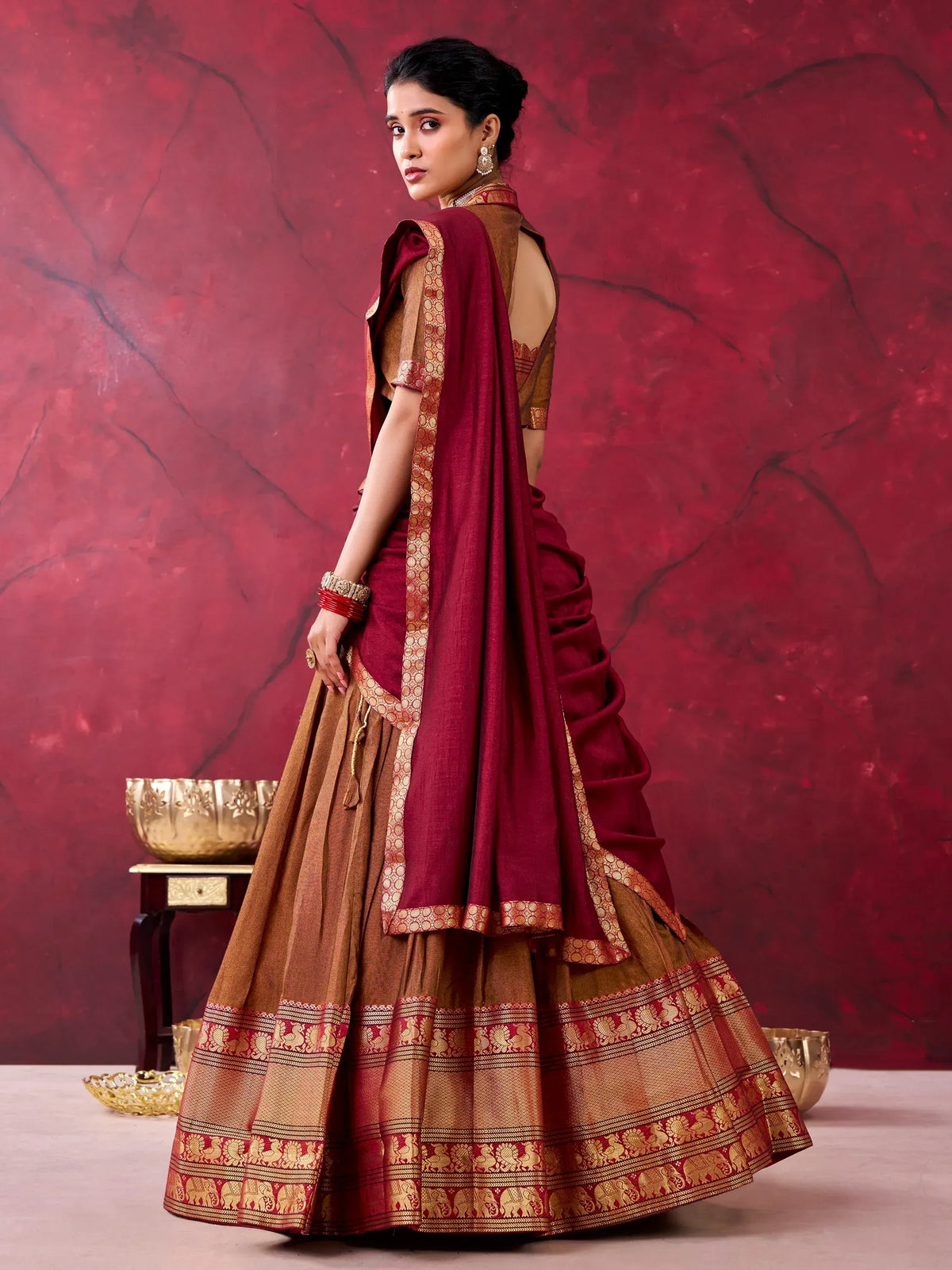 Woman in a maroon and brown designer lehenga choli with a gold bordered dupatta