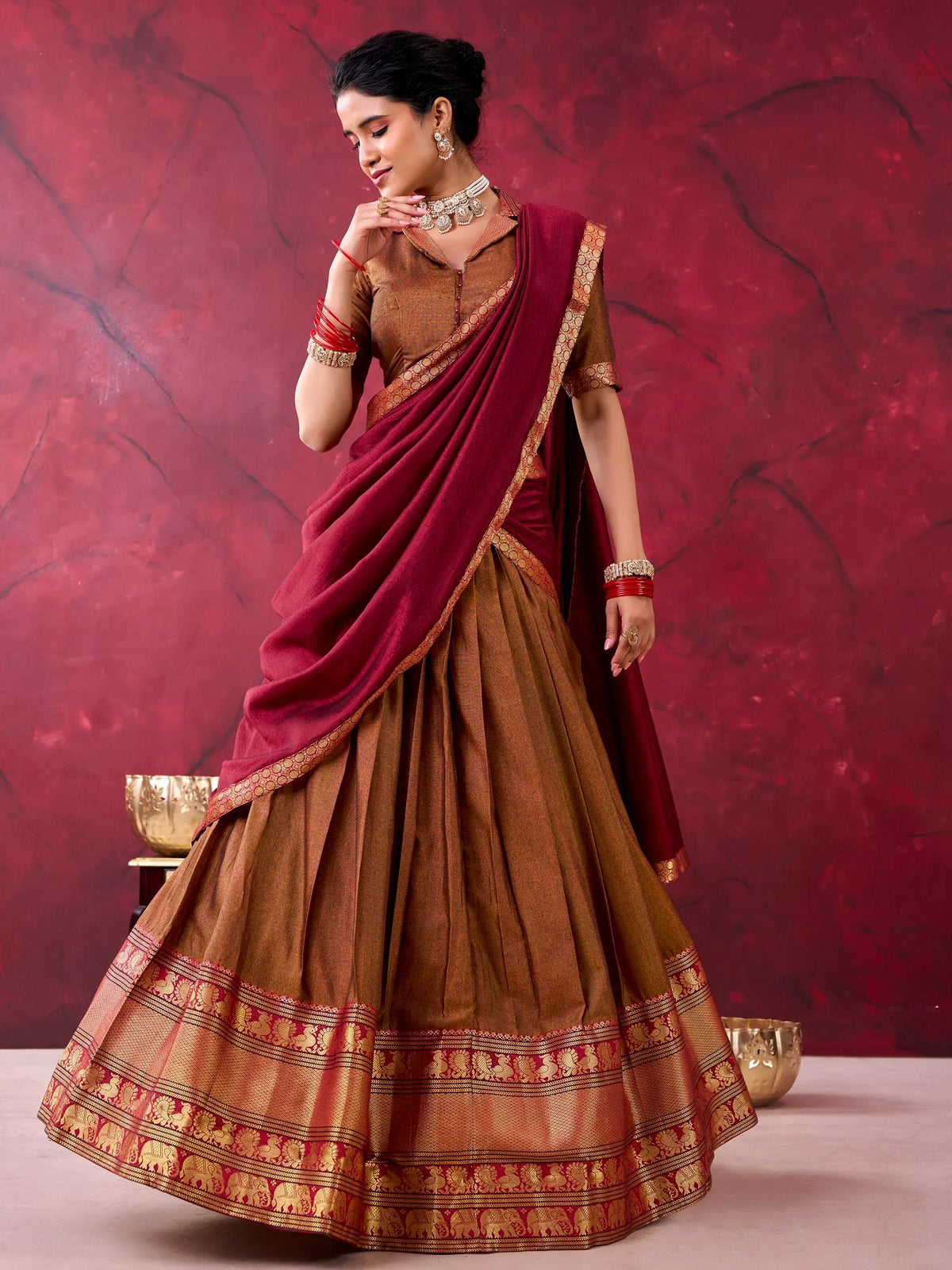 Woman wearing a brown and maroon designer lehenga choli with golden zari border
