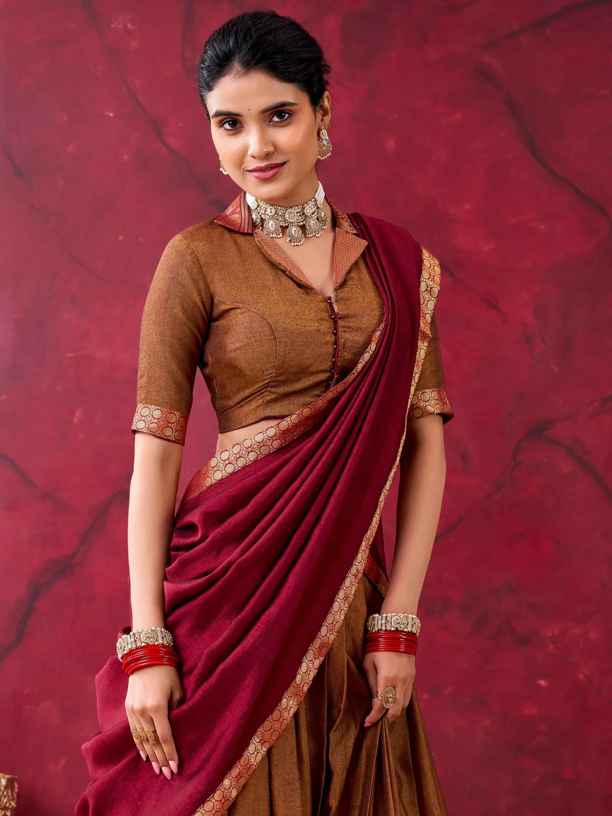 Woman in a brown collared blouse and maroon saree with traditional Indian jewelry