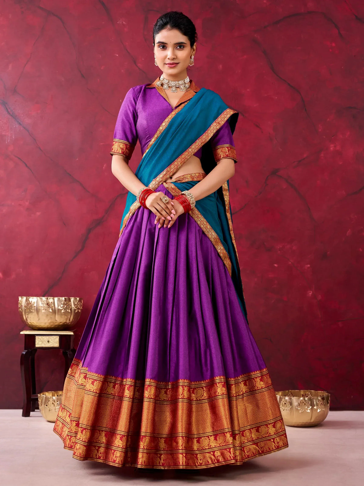 Woman wearing a purple and teal designer lehenga choli with gold zari border.