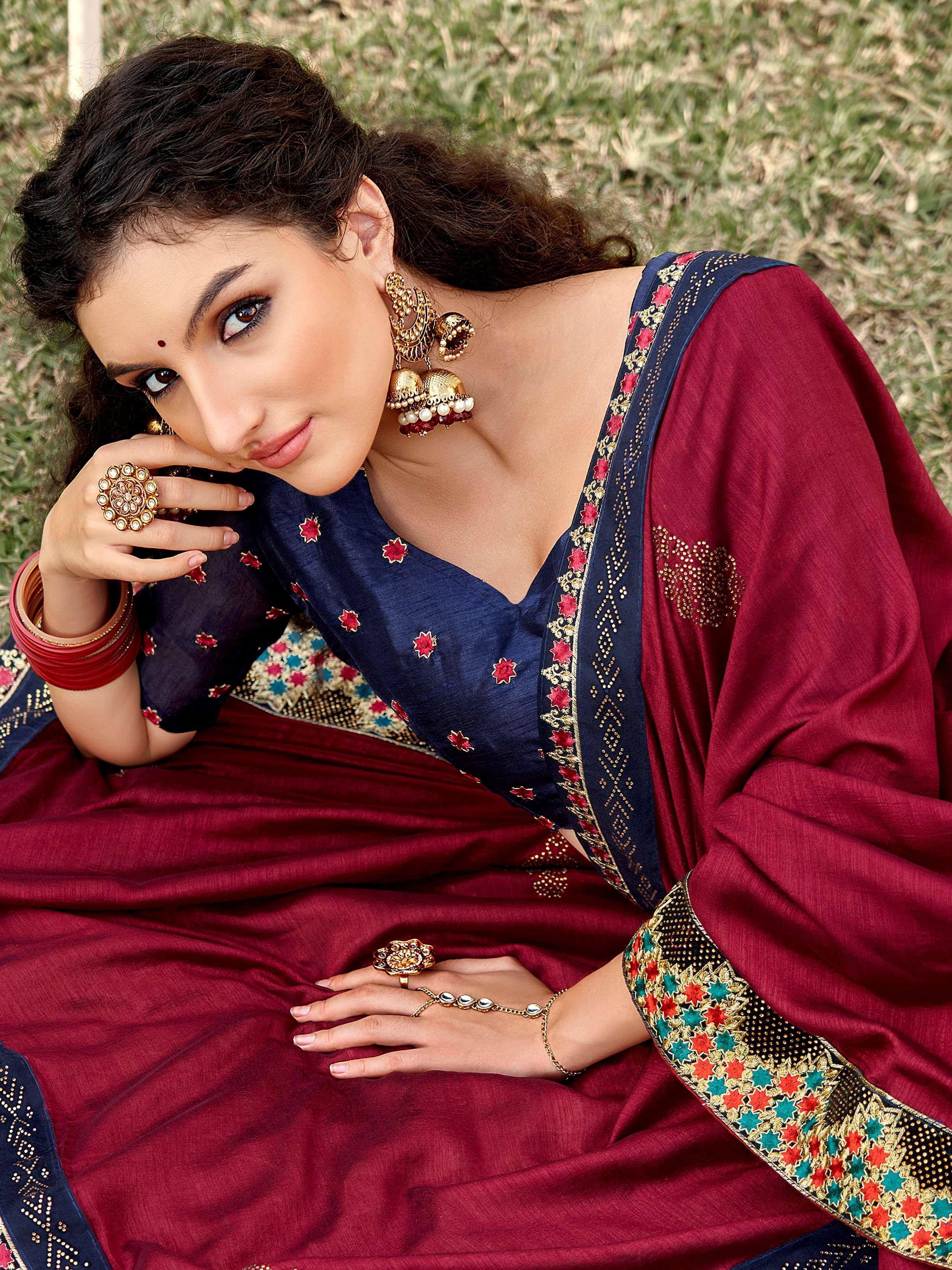 Woman in maroon and navy blue embroidered saree with gold jewelry, lying on grass