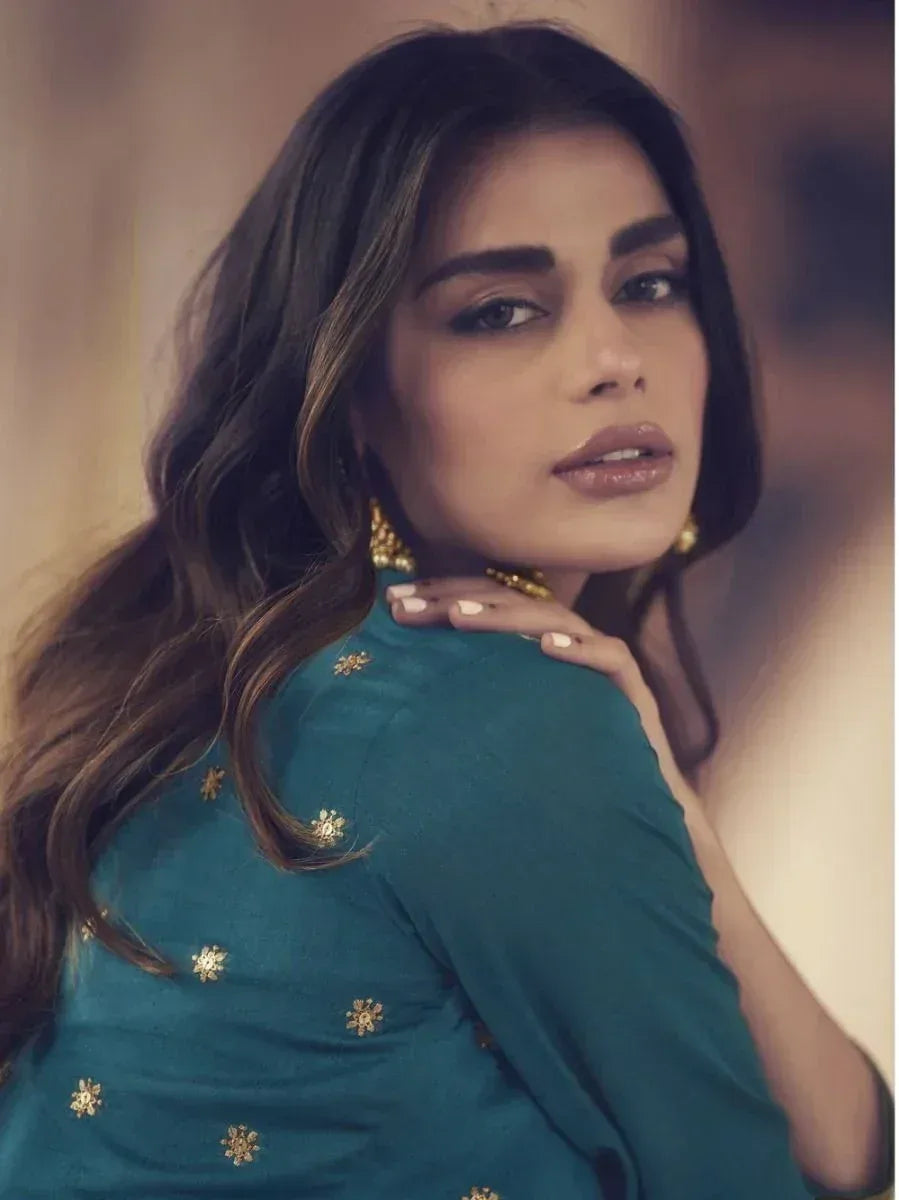 Woman in teal ethnic top with gold floral embroidery, styled with gold jewelry for festive occasions