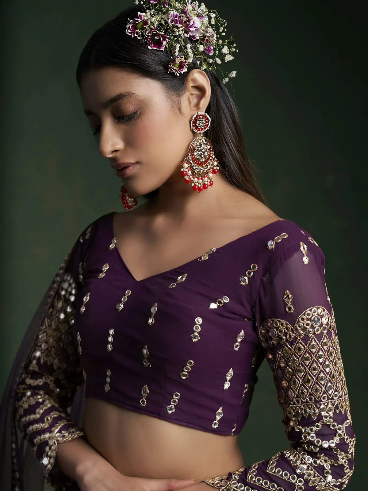 Purple ethnic blouse with mirror work, floral hair accessory, and red gold jhumka earrings