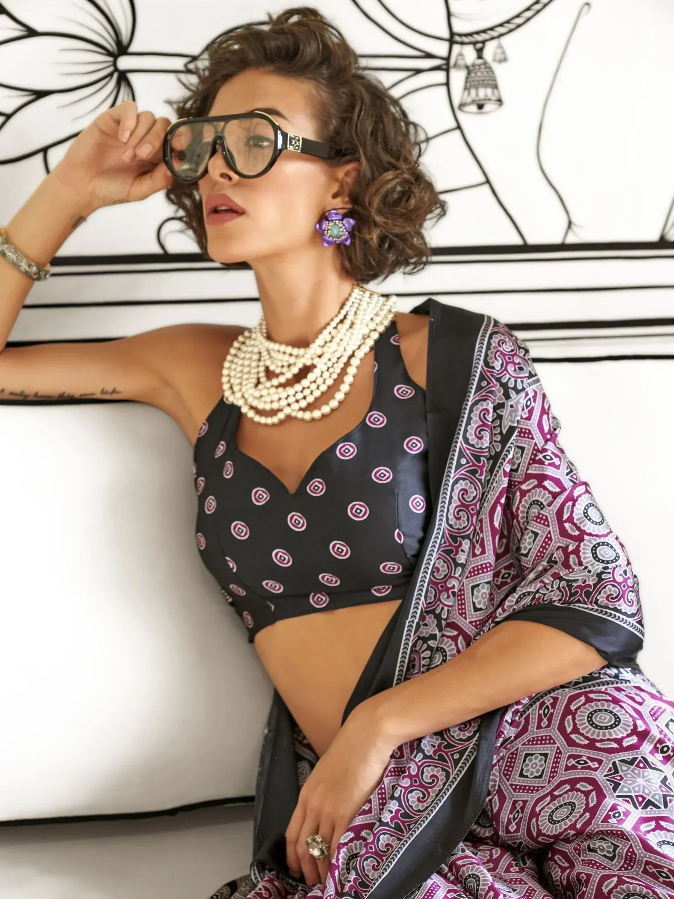 Stylish woman in black and purple printed saree with pearl necklace and bold sunglasses