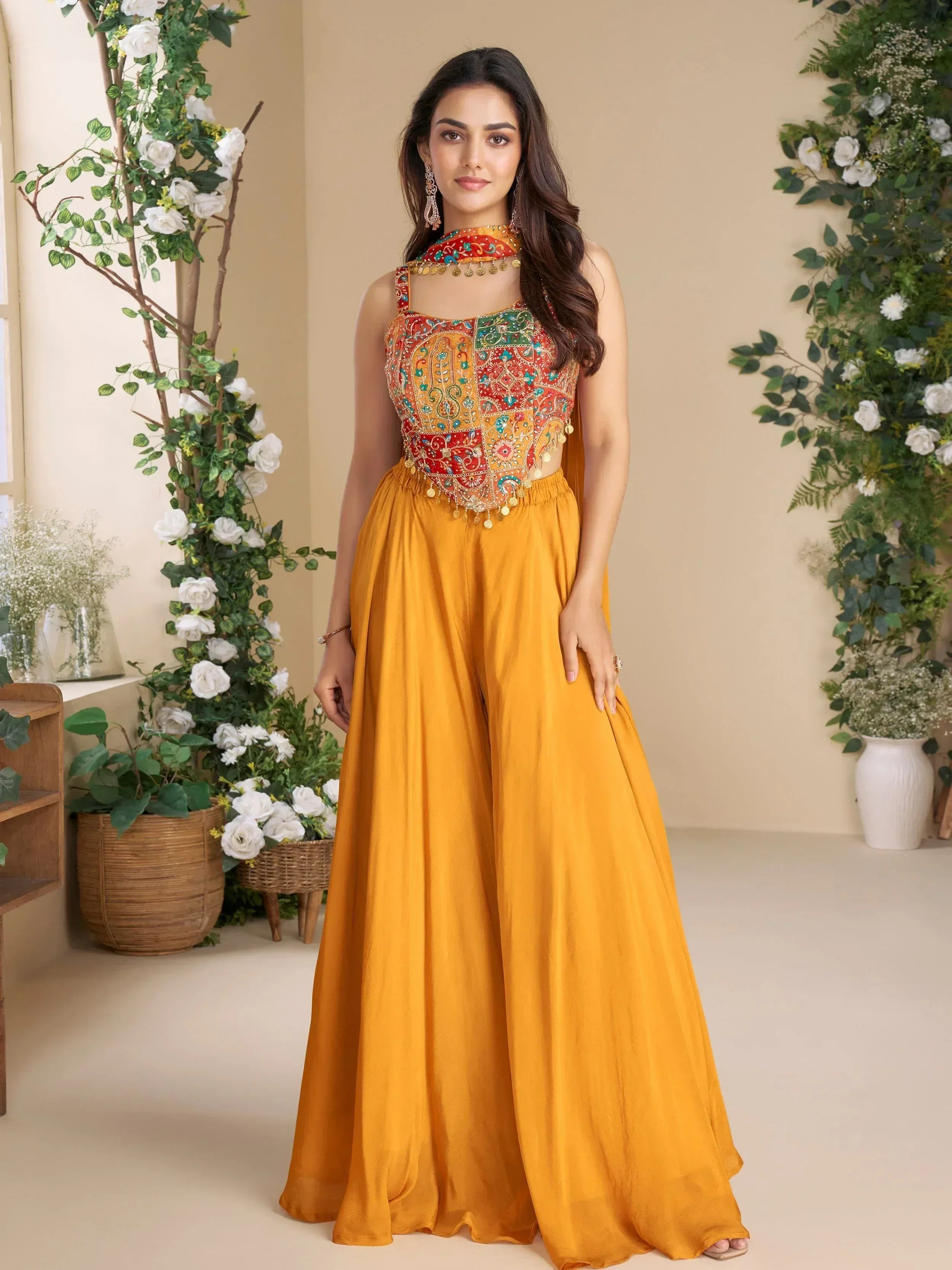 Woman in vibrant yellow ethnic gown with colorful embroidered top and floral backdrop