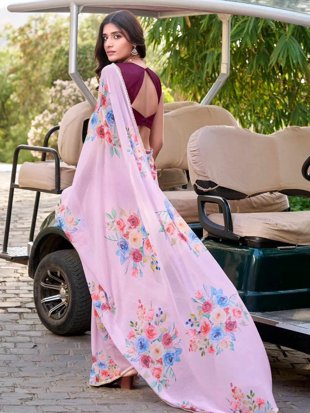 Woman in floral pink saree with maroon blouse, standing by golf cart, ethnic Indian wear