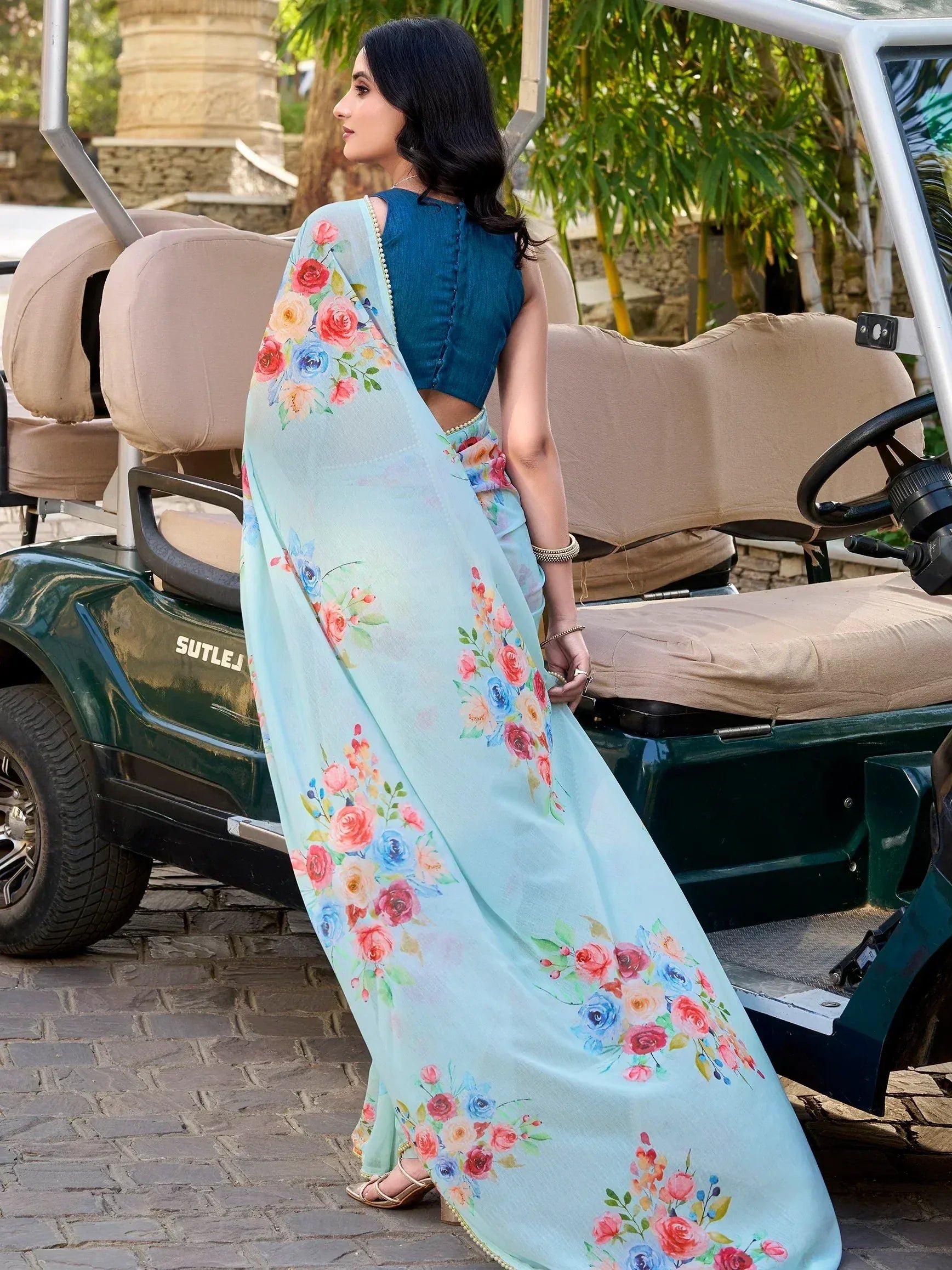 Woman in floral printed light blue saree with denim blouse, standing beside golf cart