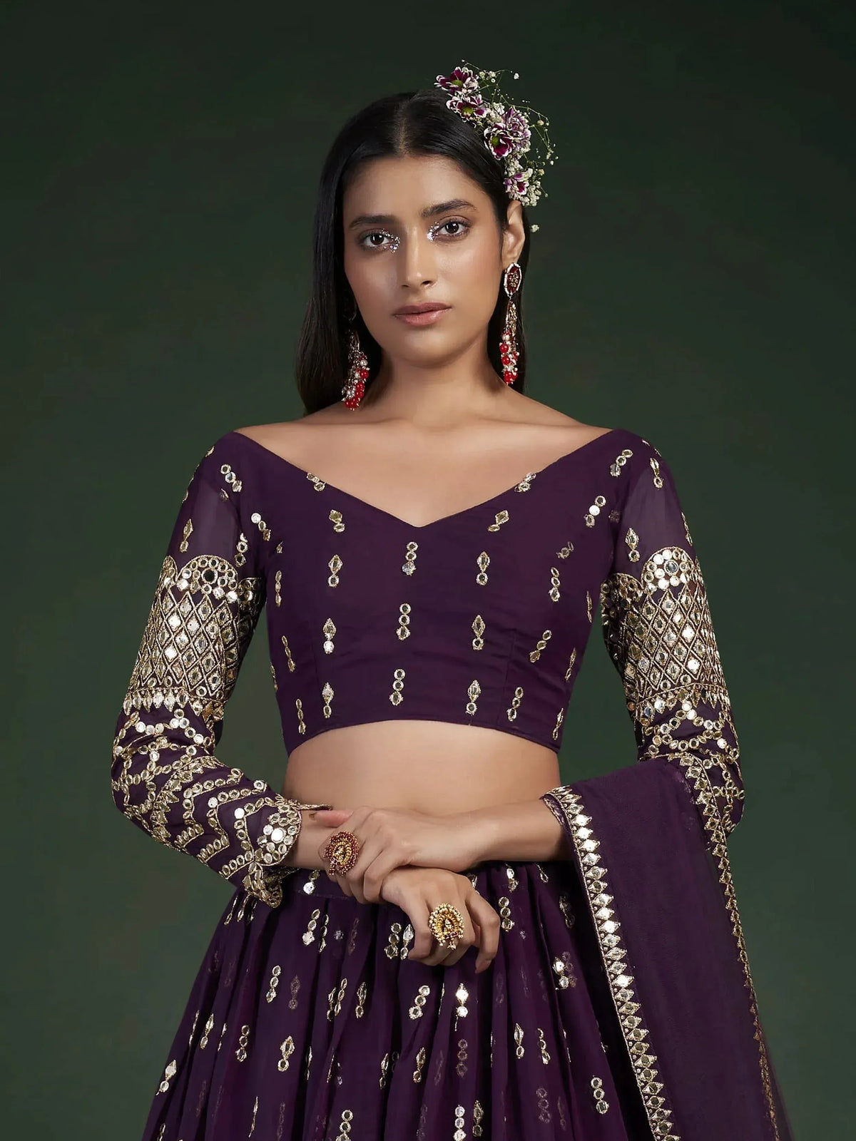 Purple designer lehenga choli with gold mirror work, floral hair accessory, and statement earrings for ethnic wear.