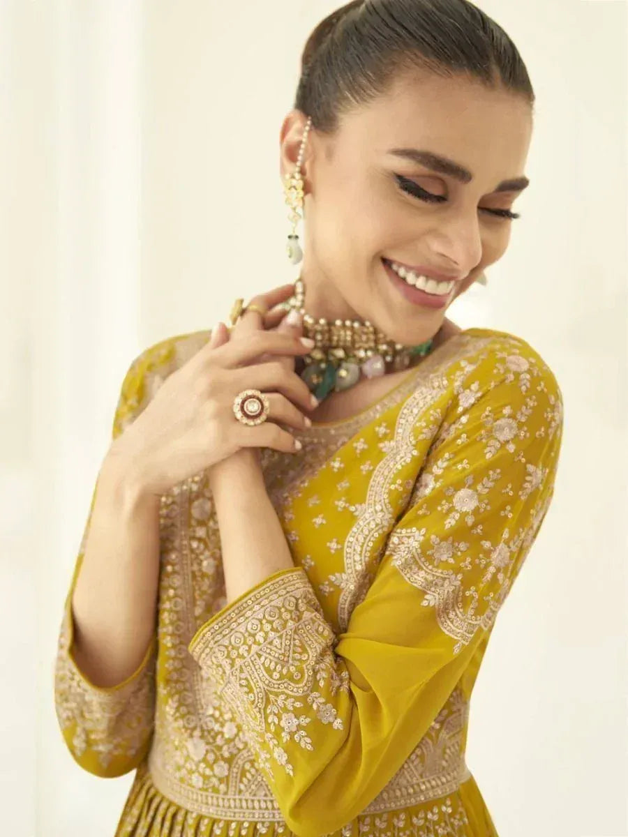 Woman in mustard yellow embroidered ethnic gown with traditional jewelry, smiling