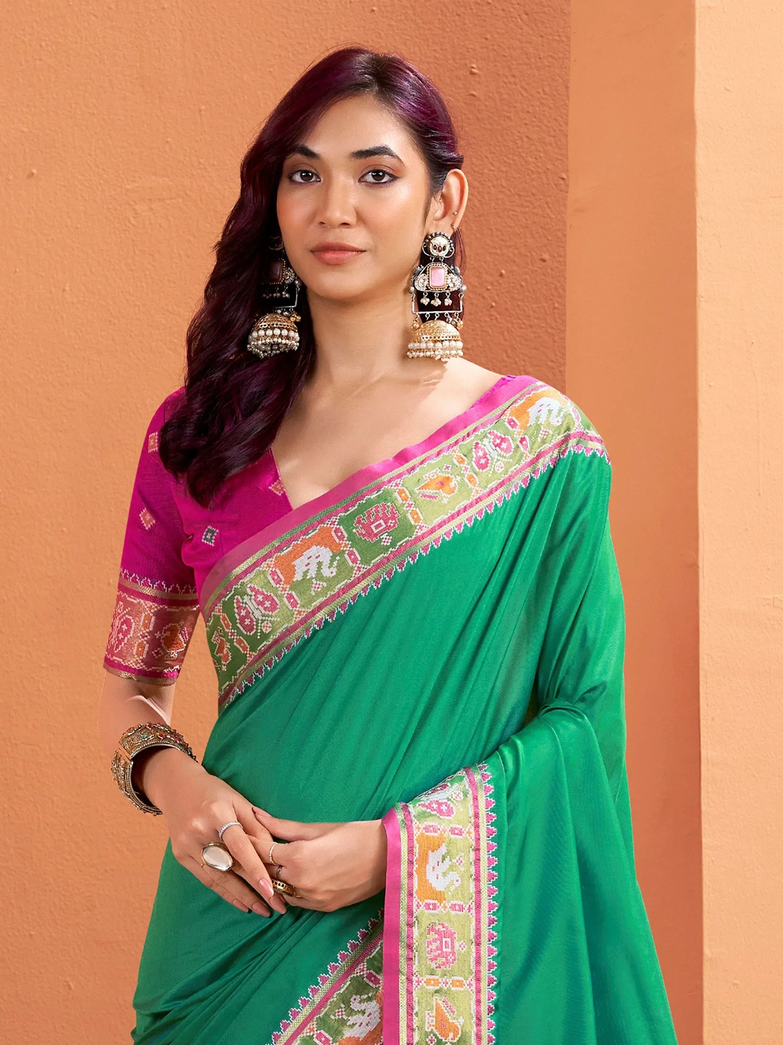 Green saree with pink border and elephant motifs, paired with matching blouse and jhumka earrings