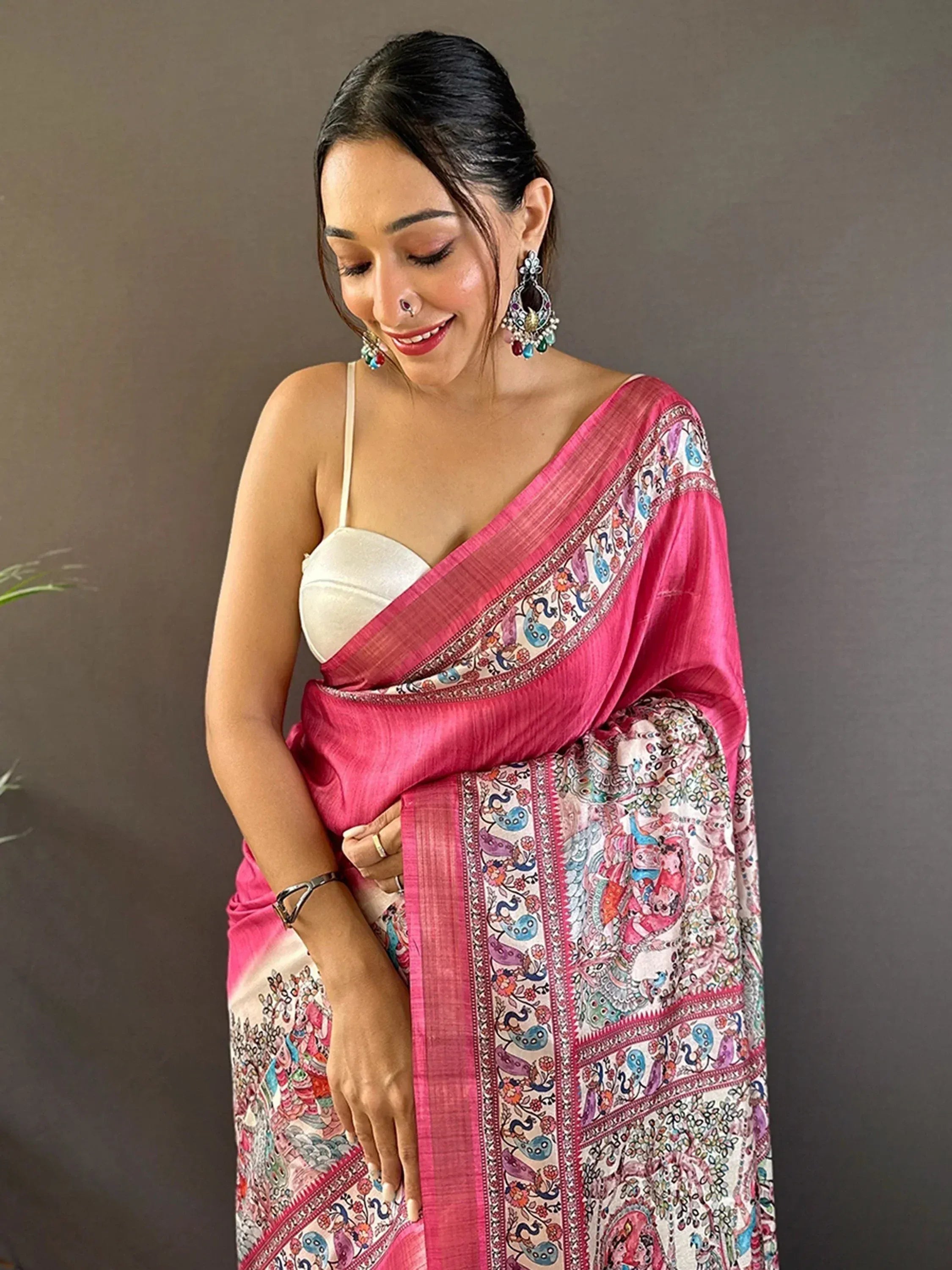 Woman in vibrant pink printed saree with peacock motifs, styled with white blouse and ethnic jewelry