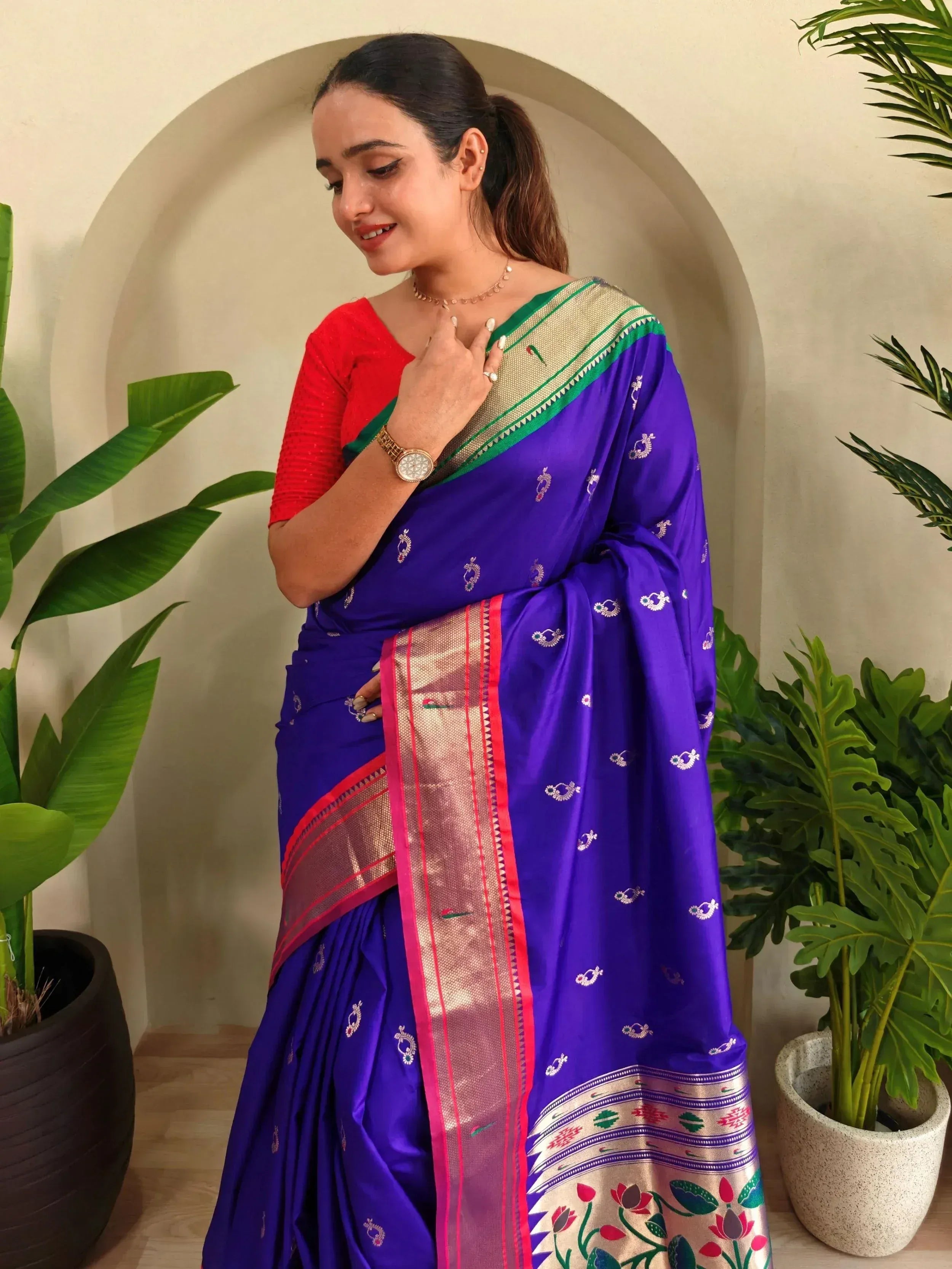 Woman in vibrant purple silk saree with gold border and floral motifs, paired with red blouse, ideal for Indian ethnic occasions.