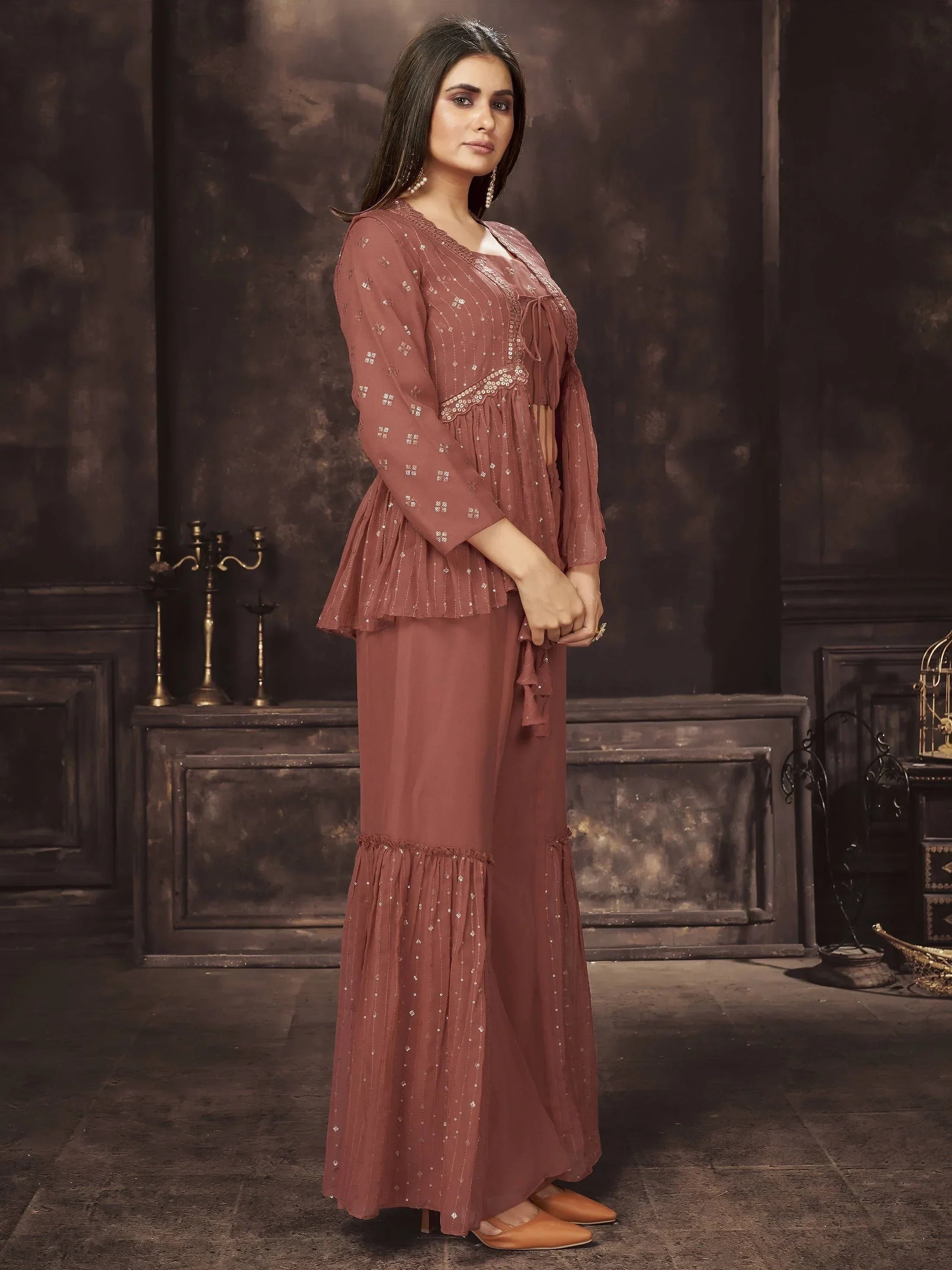 Woman in brown ethnic sharara suit with long sleeves and sequin detailing, posing indoors