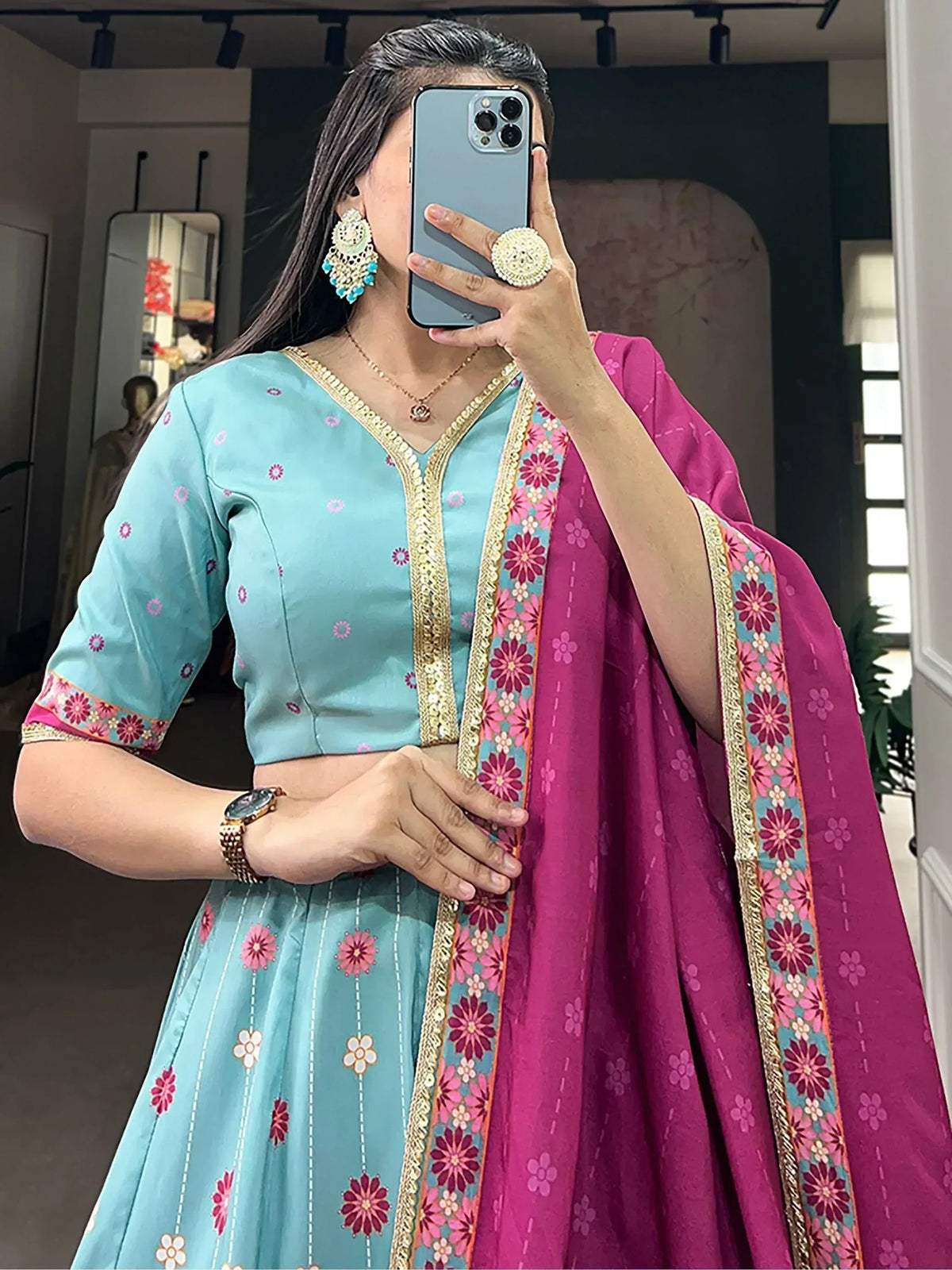 Woman wearing turquoise floral lehenga choli with pink dupatta, gold embroidery, and statement earrings