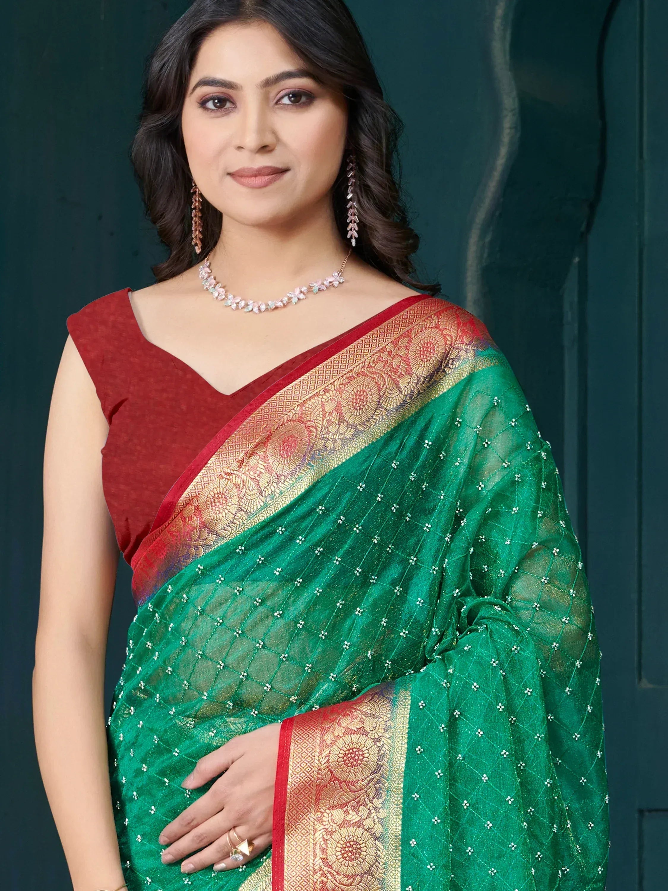Green designer saree with gold border, paired with red blouse and floral jewelry