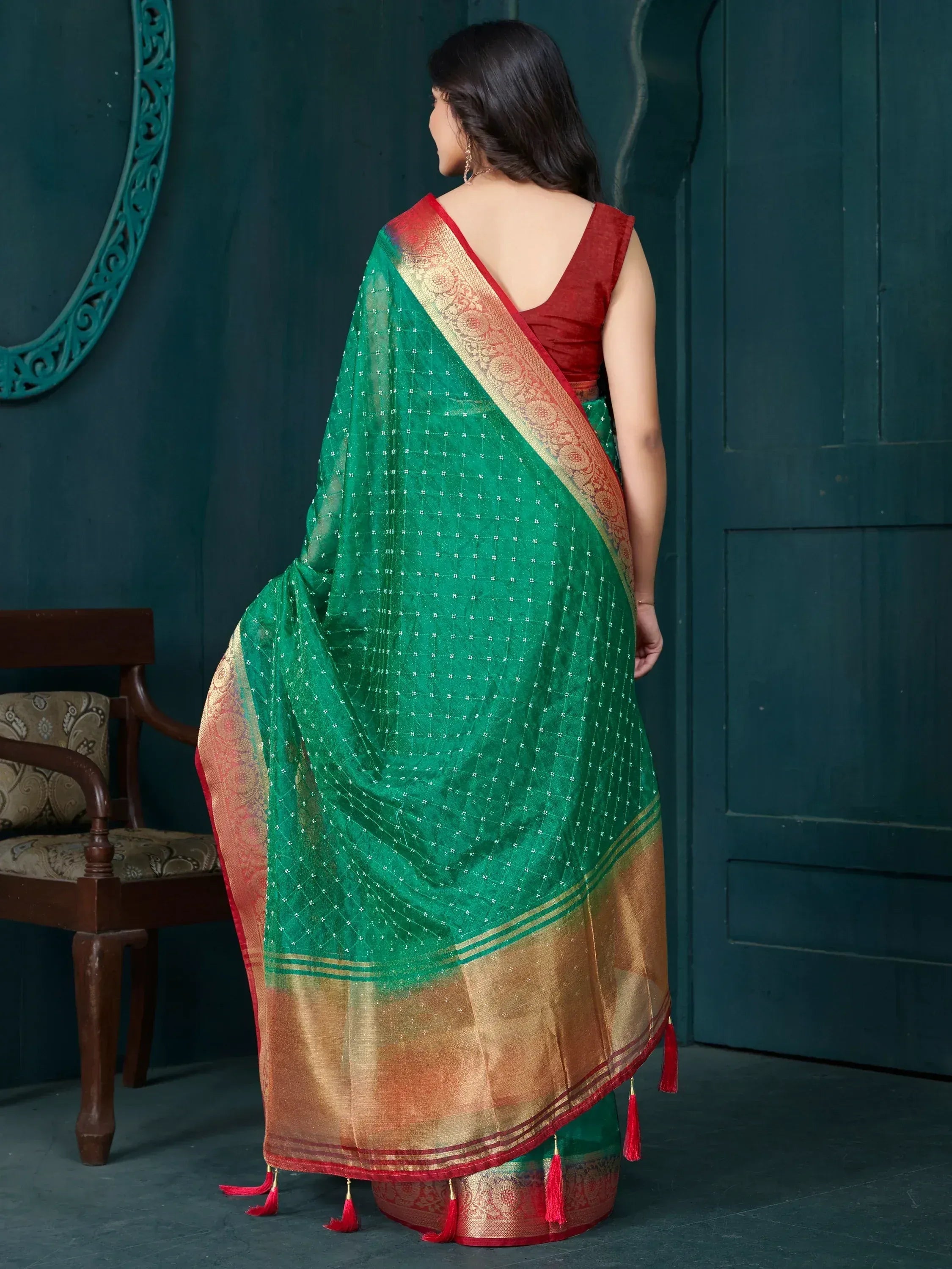 Green ethnic saree with gold border and red tassels, paired with red blouse, showcasing traditional Indian wear.