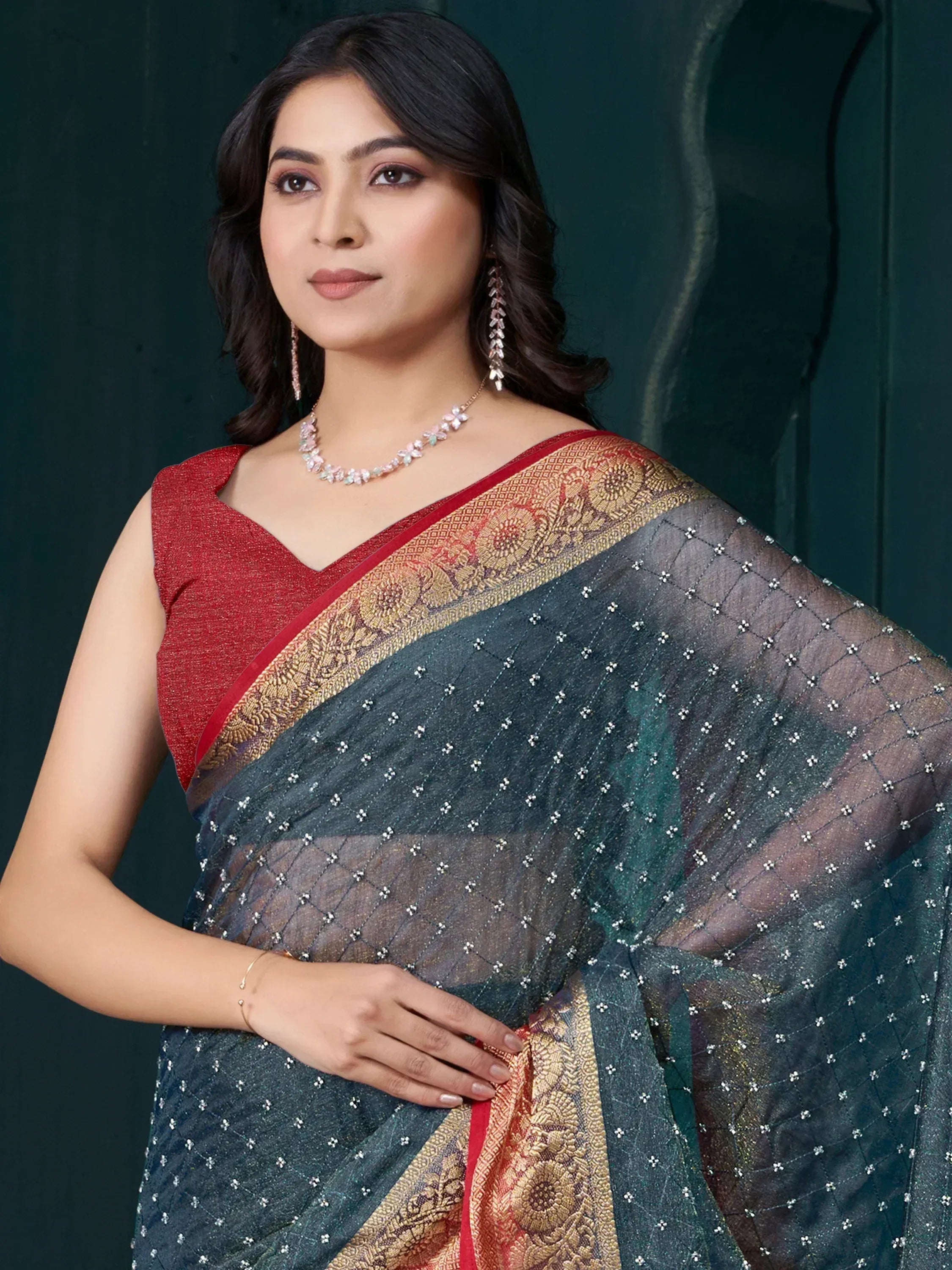 Elegant woman in dark green saree with gold border and red blouse, adorned with floral jewelry.