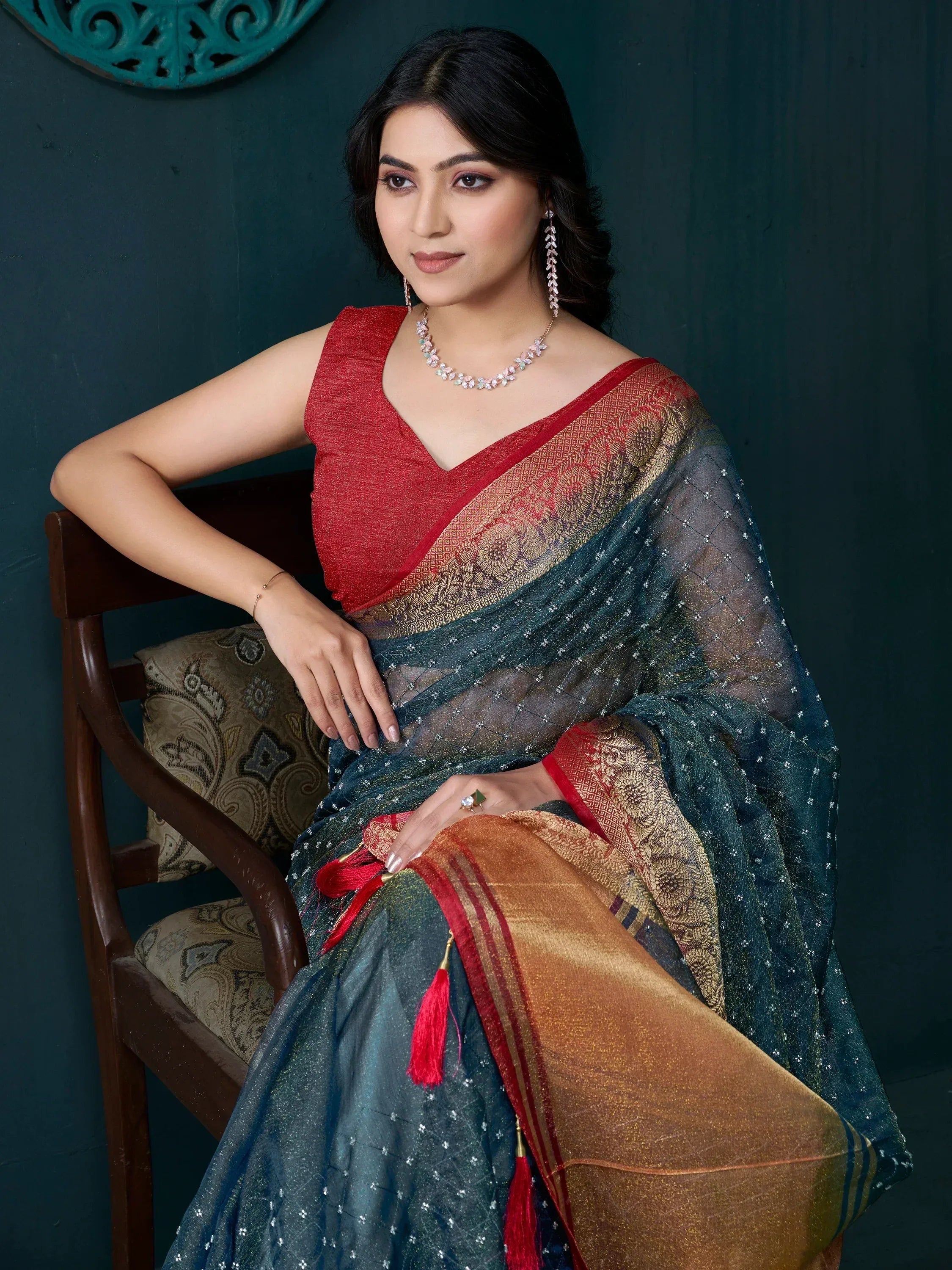 Elegant woman in designer saree with red blouse, gold embroidery, and tassels, styled for Indian ethnic wear.
