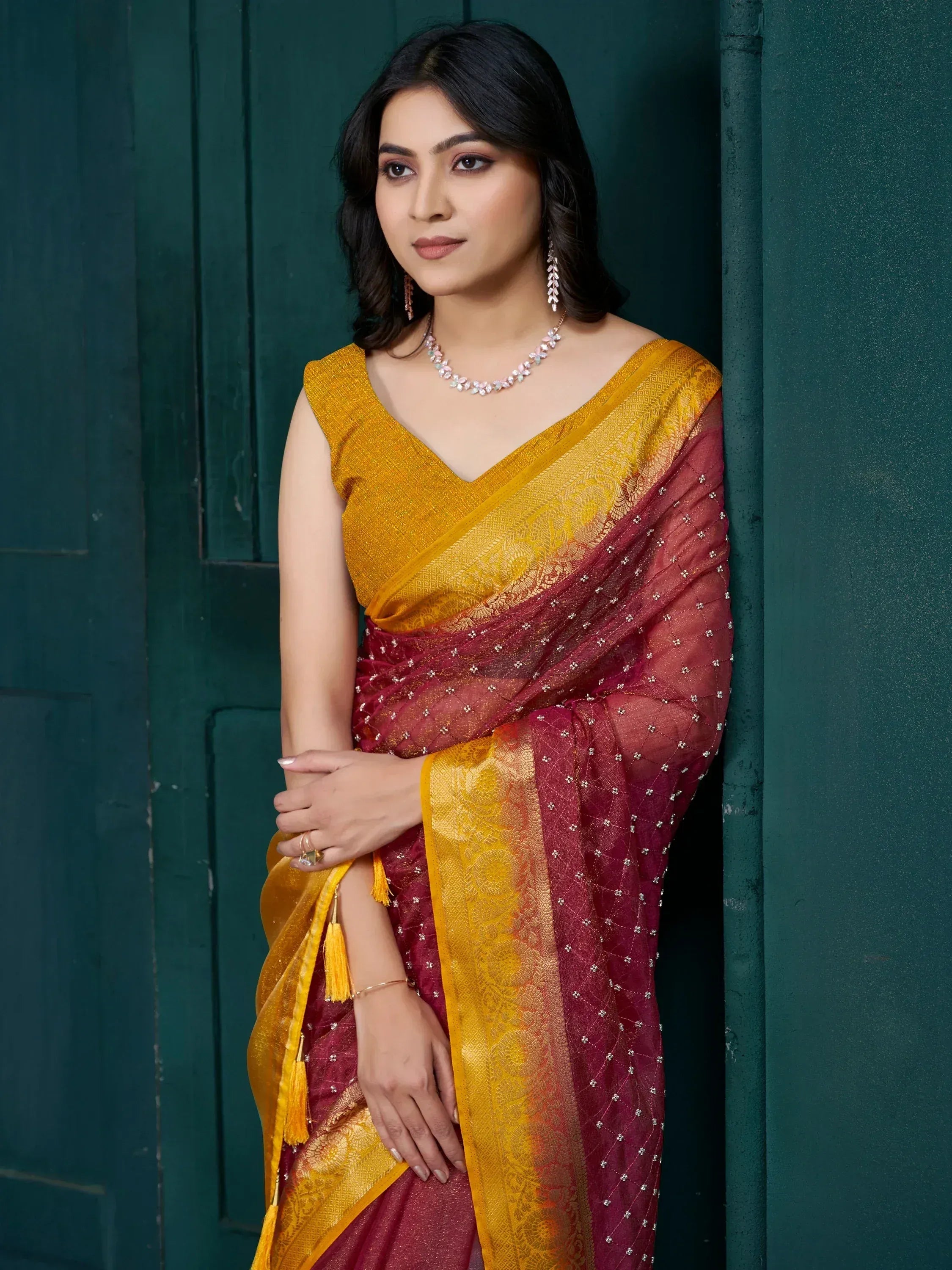 Elegant maroon and gold saree with intricate embroidery and tassels, paired with matching jewelry.