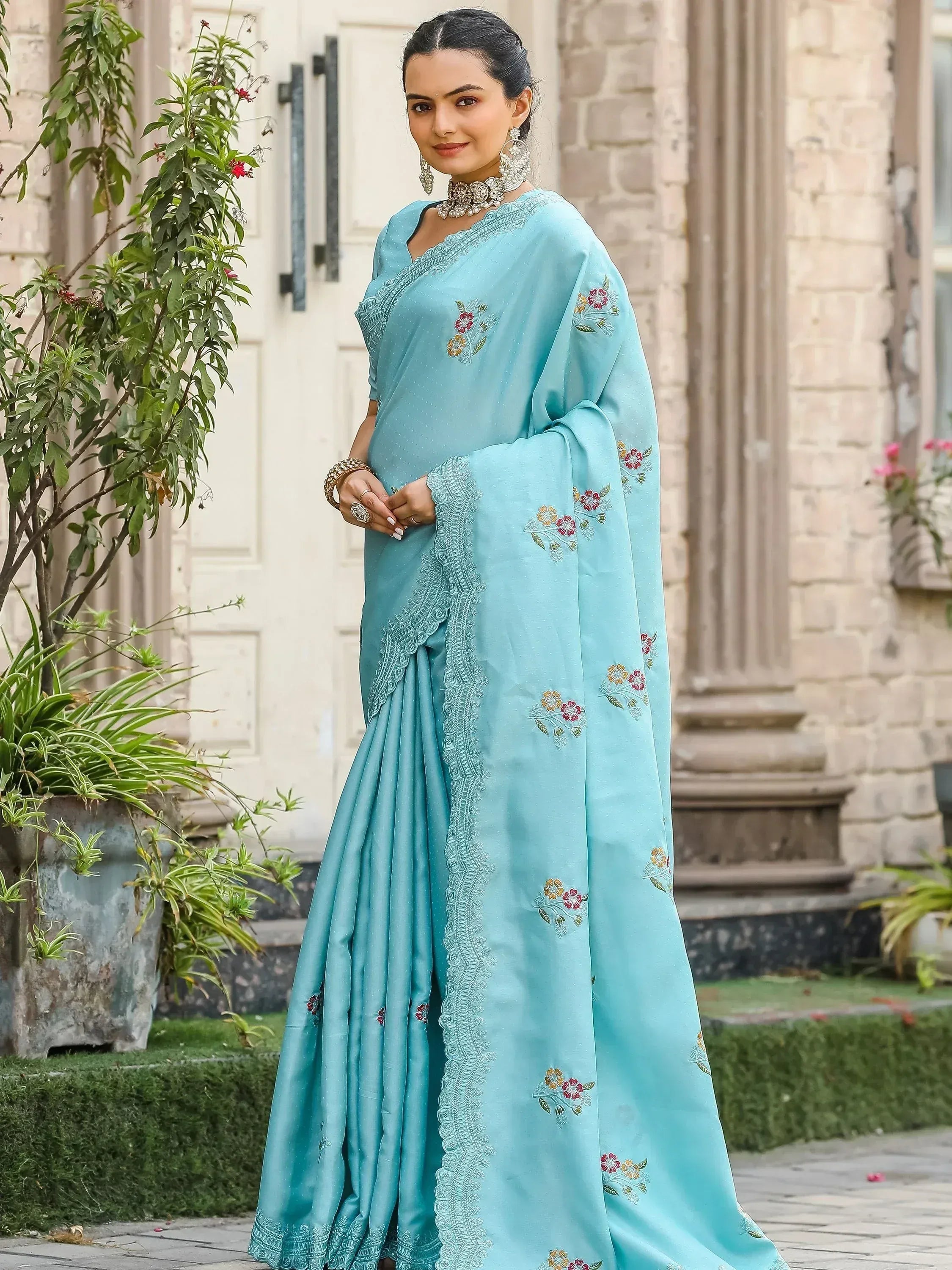 Light blue embroidered saree with floral motifs and lace border, styled with traditional jewelry