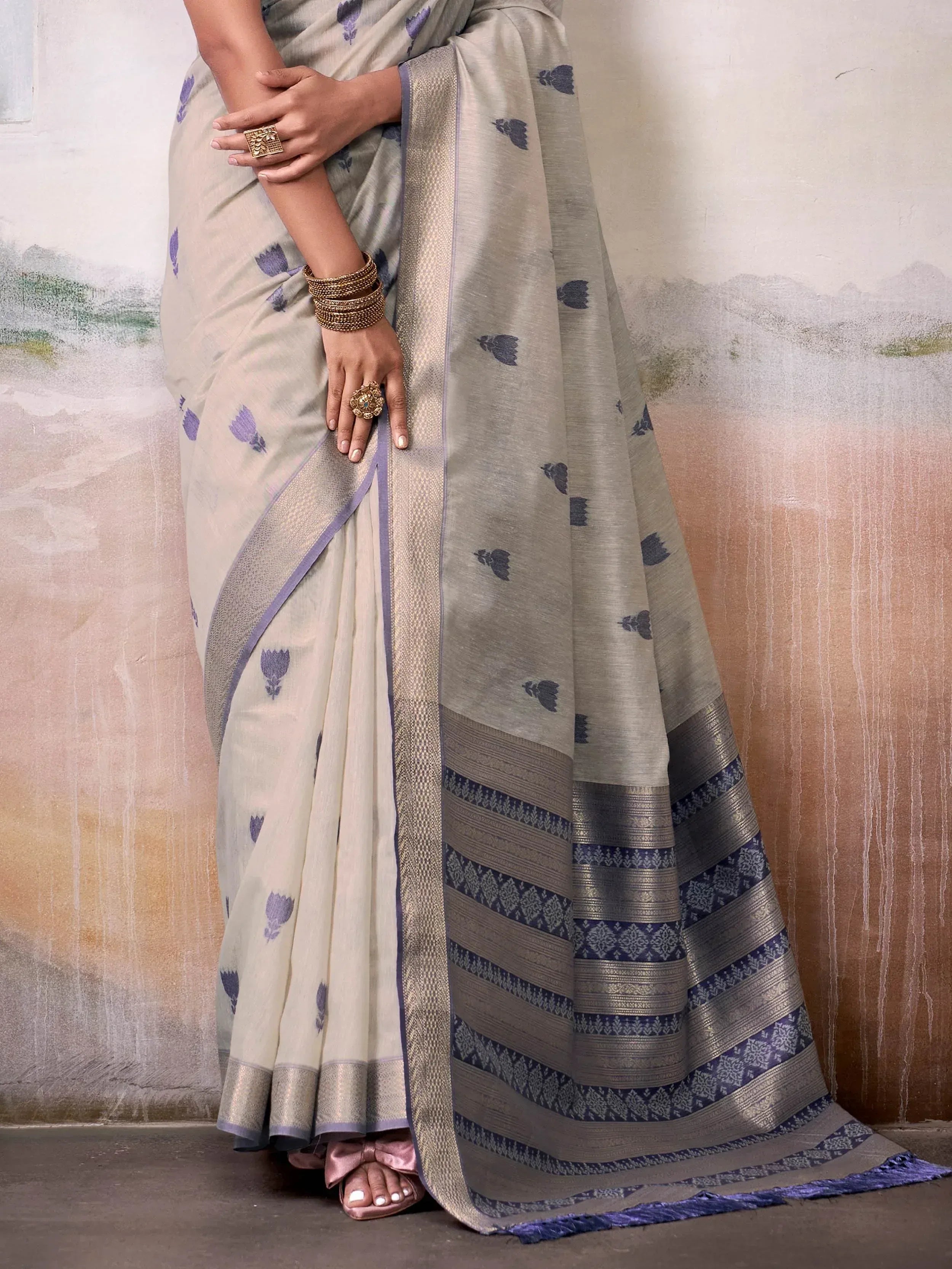 Elegant beige saree with purple floral print and woven border, styled with gold jewelry for Indian ethnic wear