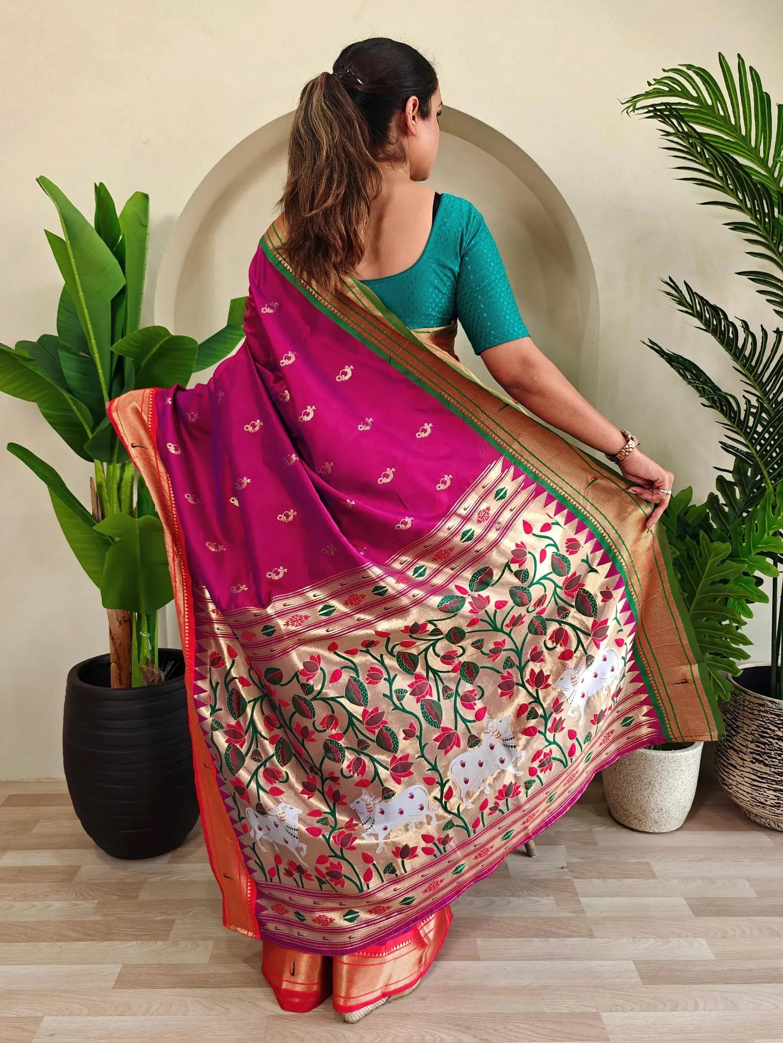 Woman in vibrant pink and gold ethnic saree with floral and cow motifs, paired with teal blouse, ideal for festive occasions.