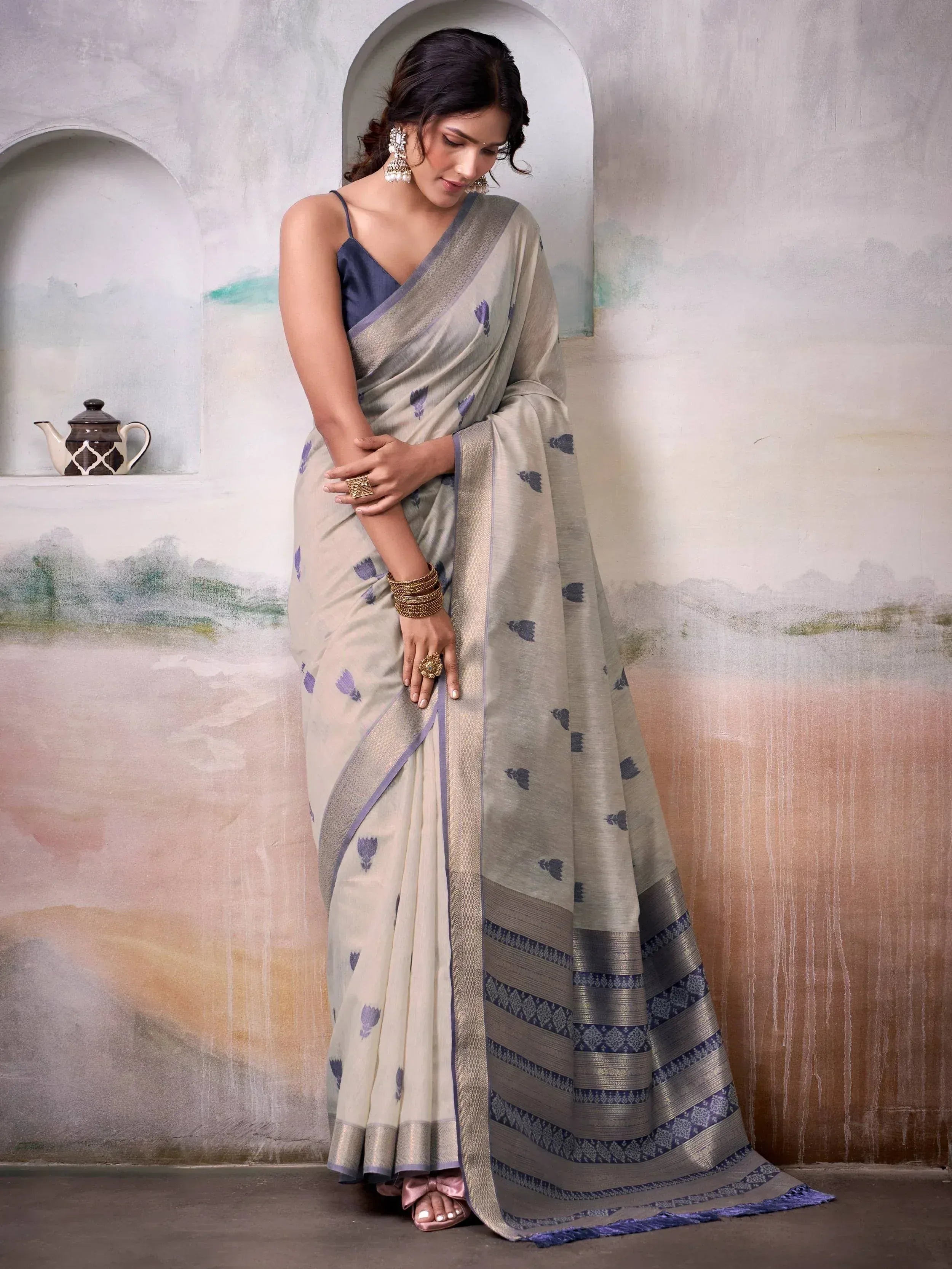 Woman in elegant beige saree with purple floral print and woven border, styled with gold jewelry for Indian ethnic wear