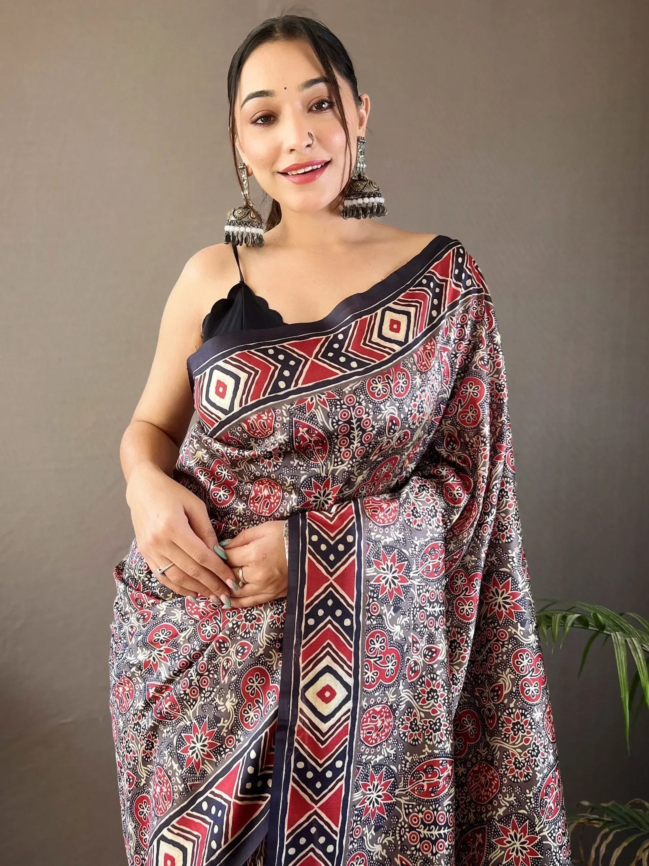 Woman in printed ethnic saree with red, black, and grey floral geometric pattern, paired with black blouse and jhumka earrings