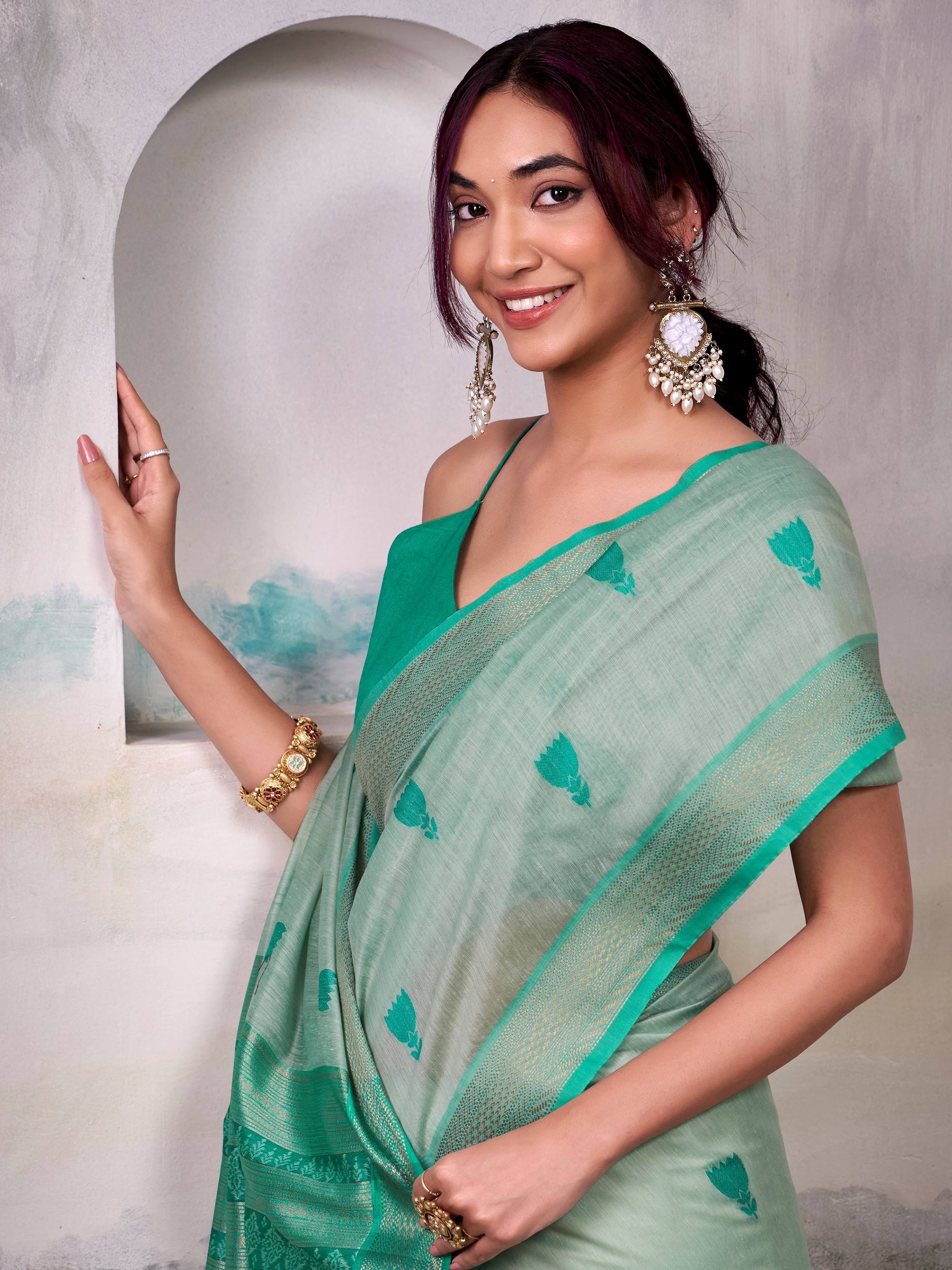 Woman in mint green saree with floral motifs and gold border, styled with statement earrings and traditional jewelry