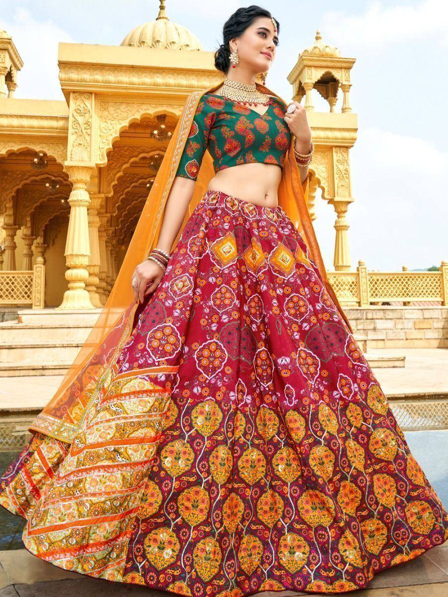 Woman in vibrant red and green printed lehenga choli with orange dupatta, standing at golden palace