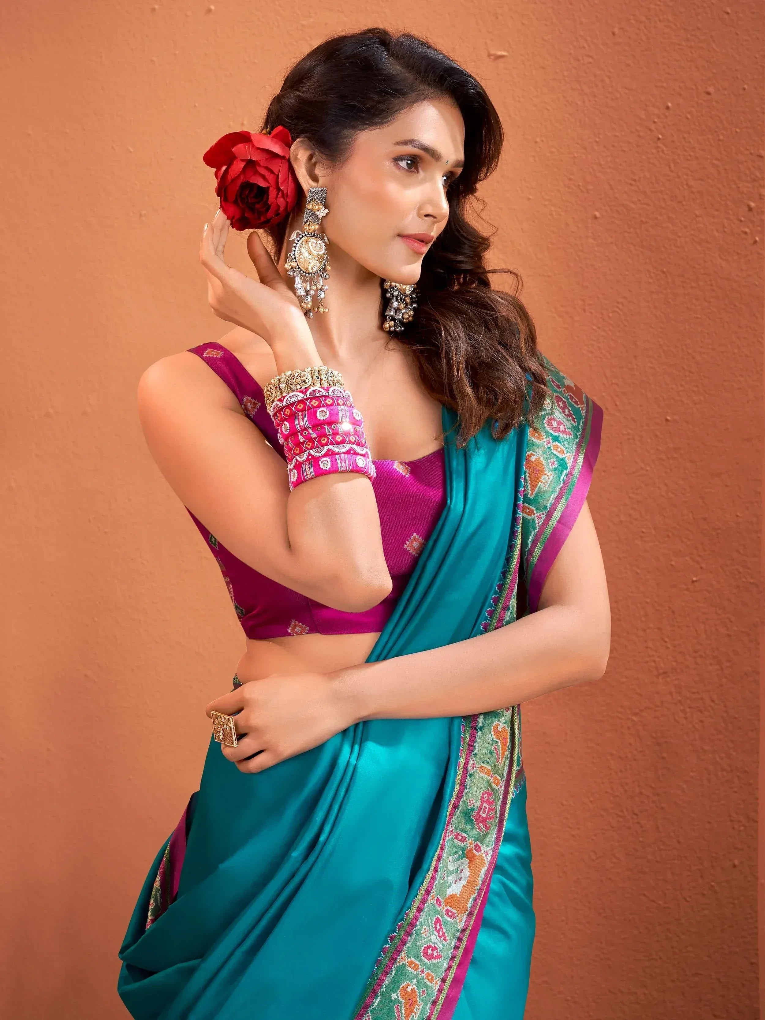 Woman in teal saree with pink blouse, ethnic jewelry, and red flower hair accessory