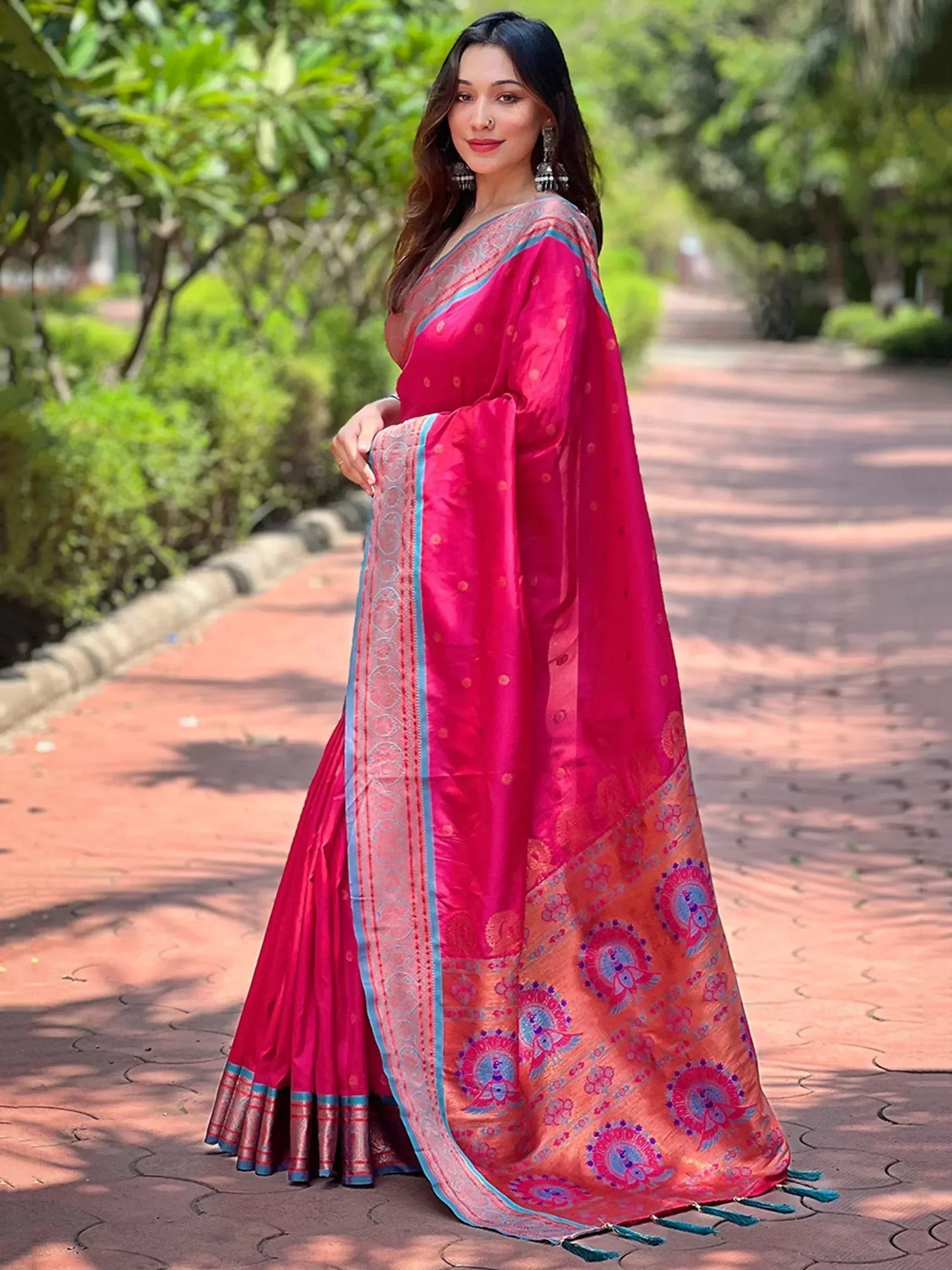 Woman in vibrant pink silk saree with blue border and peacock motifs, perfect for Indian ethnic wear occasions