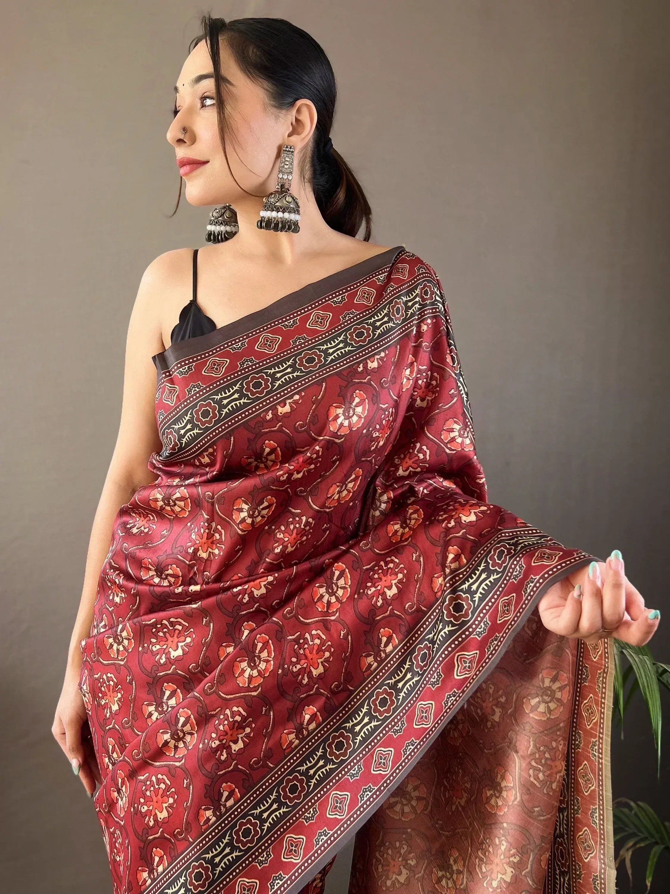 Woman in maroon floral print saree with black border, ethnic jewelry, and black blouse