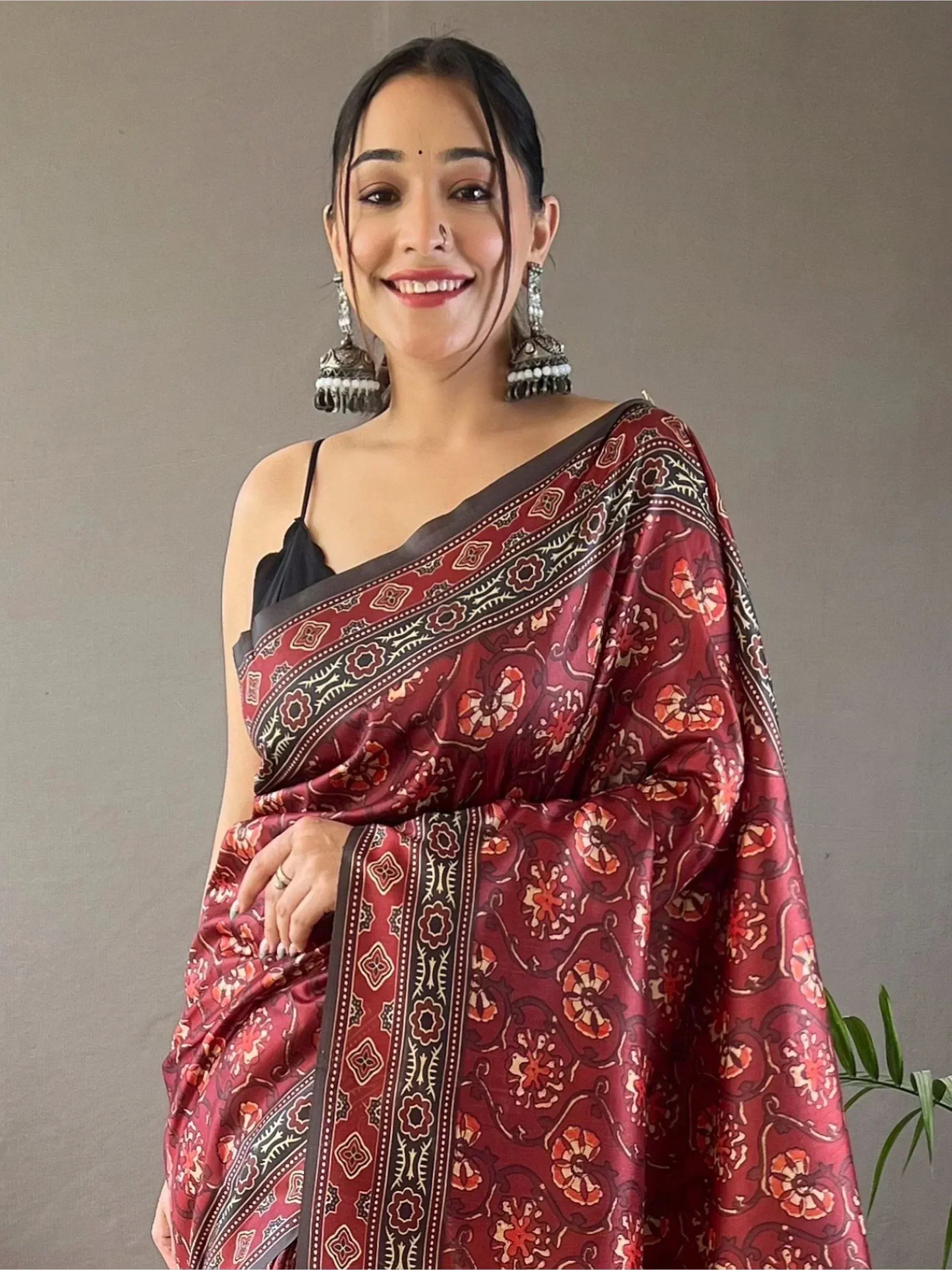Woman in maroon floral print saree with black border, styled with jhumka earrings for ethnic wear
