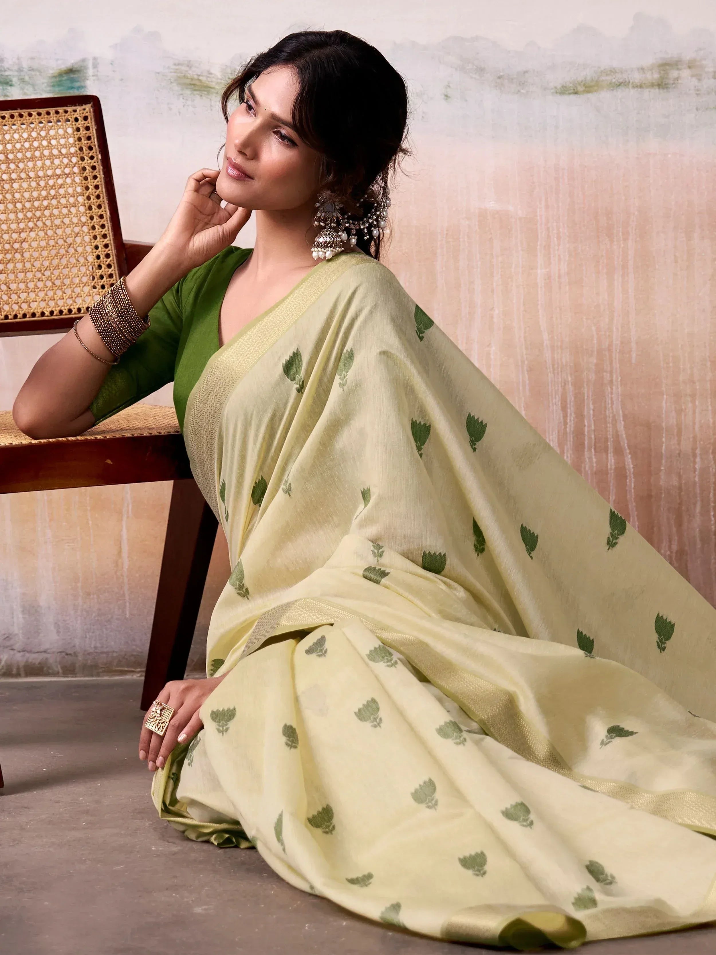 Elegant woman in light yellow saree with green floral print, paired with green blouse and traditional jewelry.