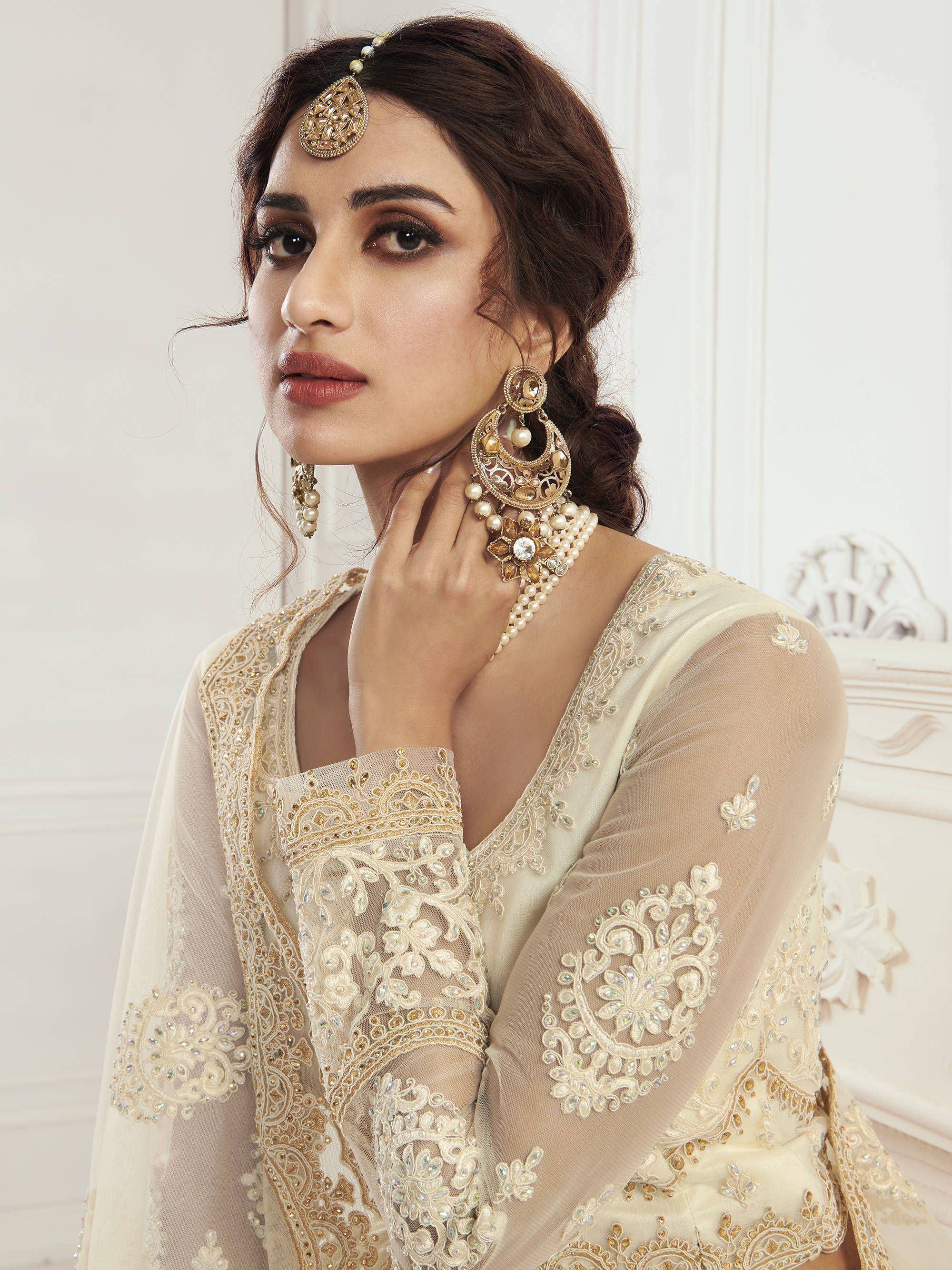 Elegant cream embroidered ethnic gown with gold jewelry, perfect for Indian weddings and festive occasions.