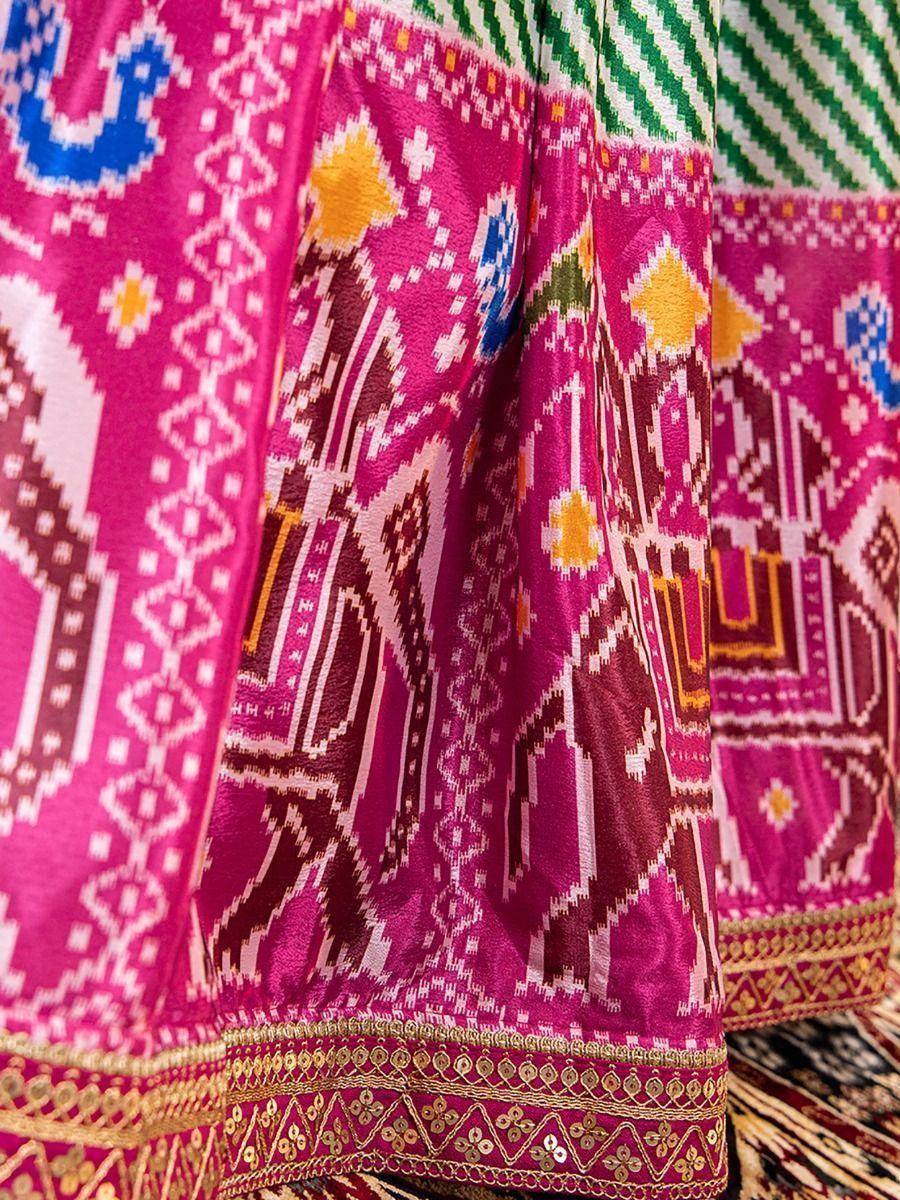 Vibrant pink ethnic gown with geometric ikat print and gold embroidery, perfect for festive occasions.