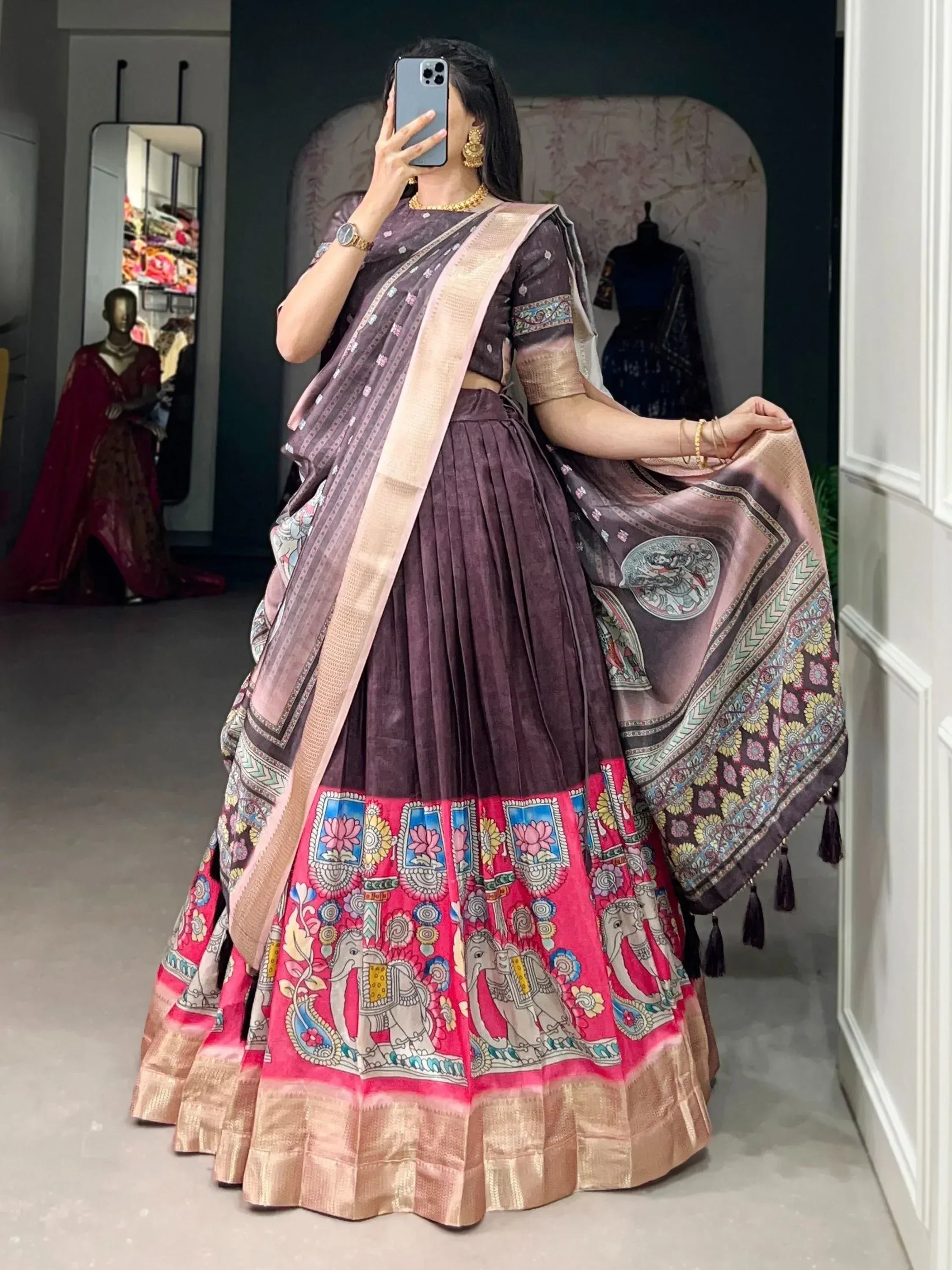 Woman in purple lehenga choli with elephant print, floral border, and gold trim, taking mirror selfie in boutique.