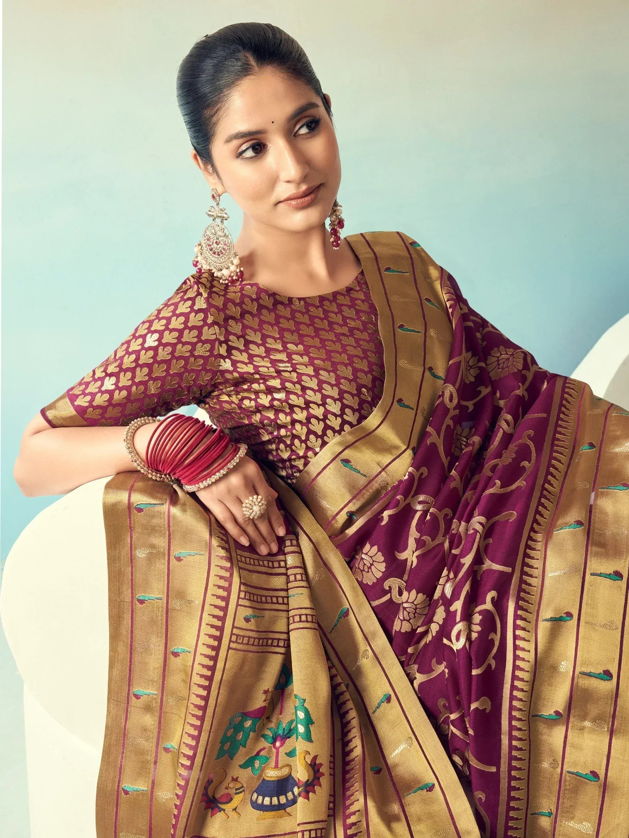 Woman in maroon and gold designer saree with intricate embroidery and traditional jewelry