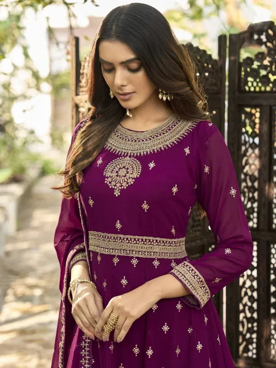 Woman wearing purple embroidered Anarkali suit with gold jewelry, outdoor backdrop