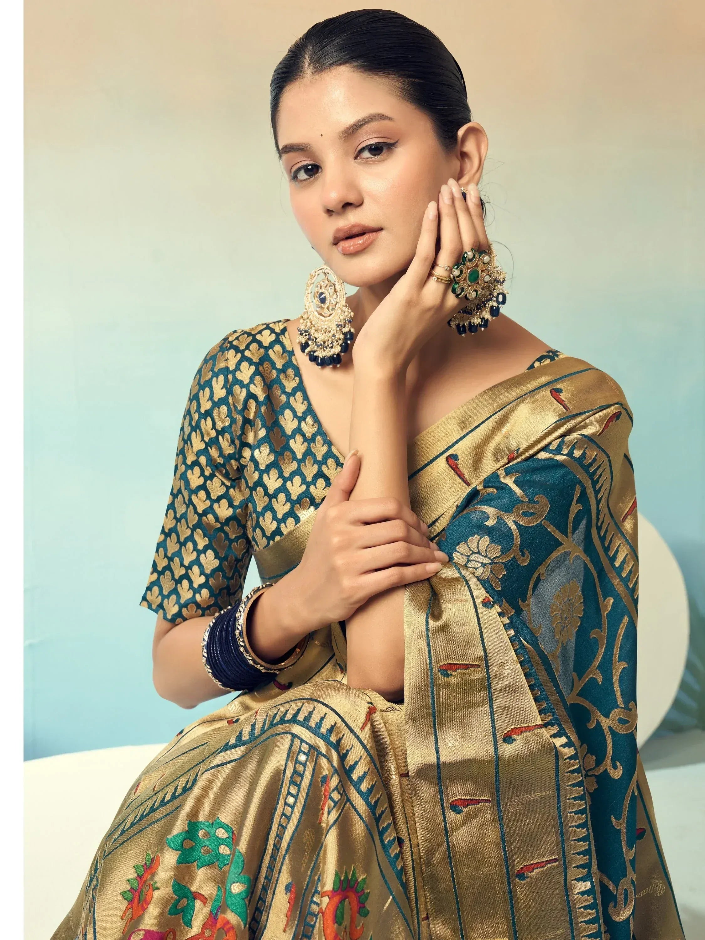 Elegant woman in teal and gold designer saree with intricate floral patterns and traditional jewelry
