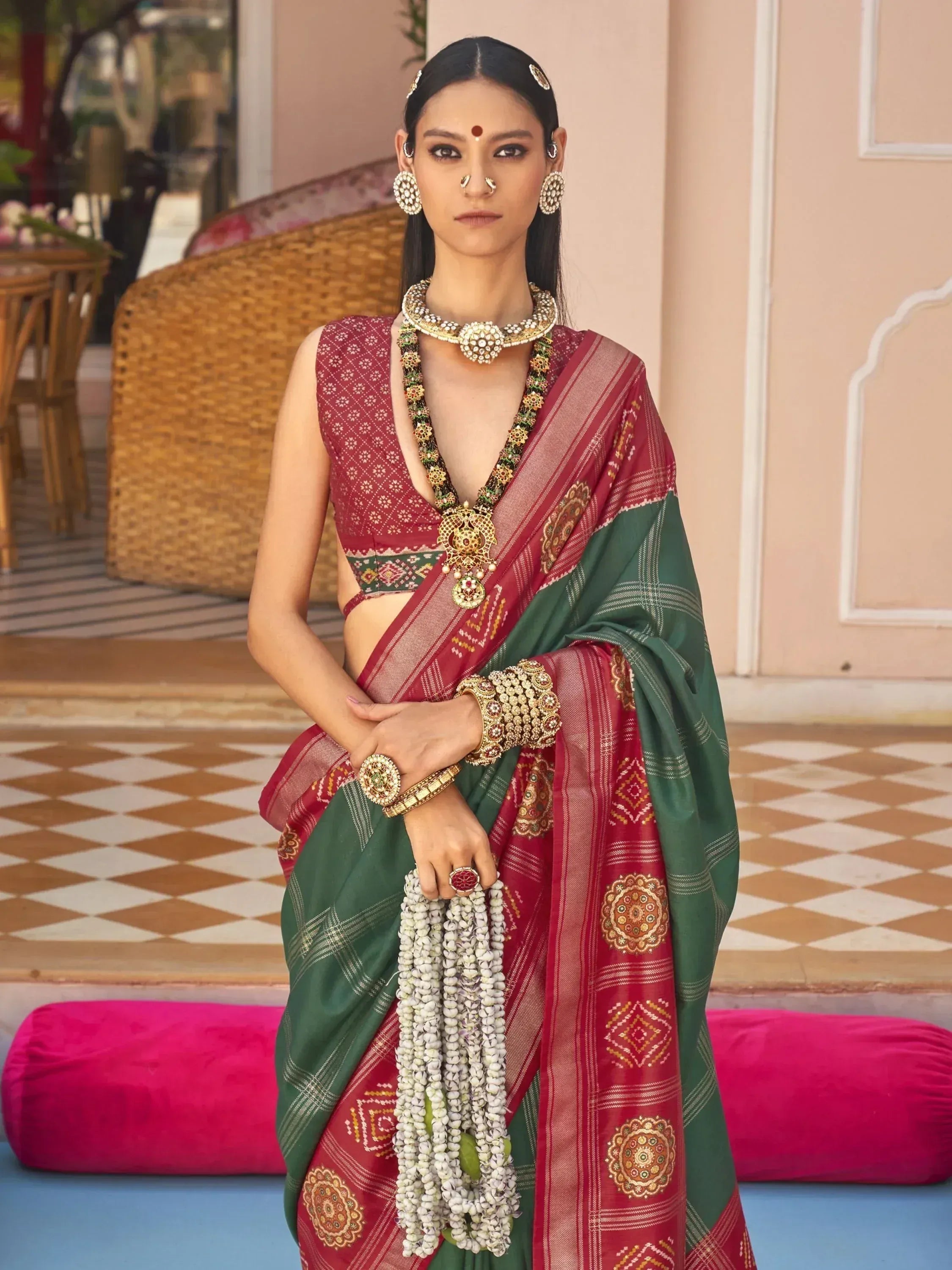 Woman in red and green ethnic saree with gold jewelry and floral garland, traditional Indian attire
