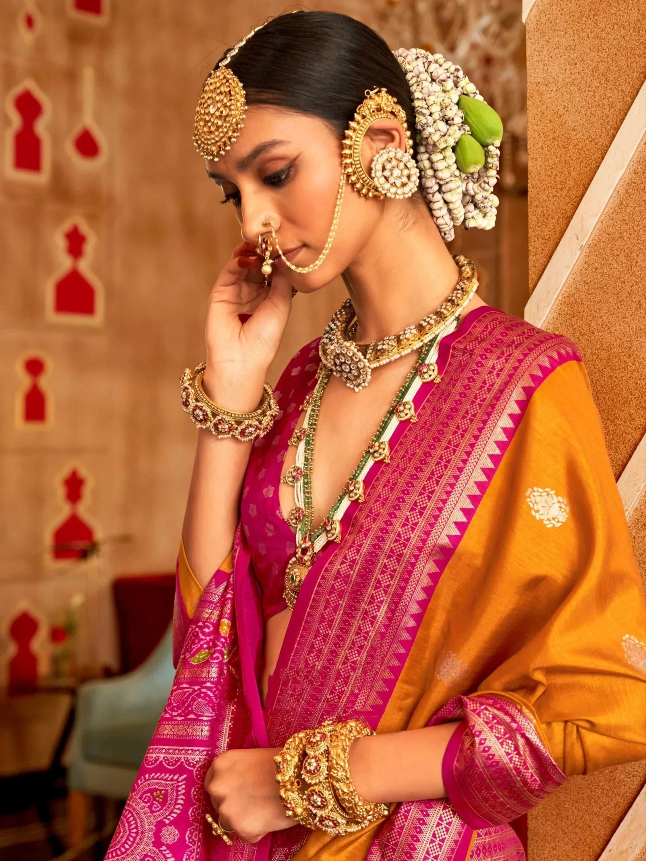 Elegant woman in pink and gold ethnic saree with traditional jewelry and floral hair adornment