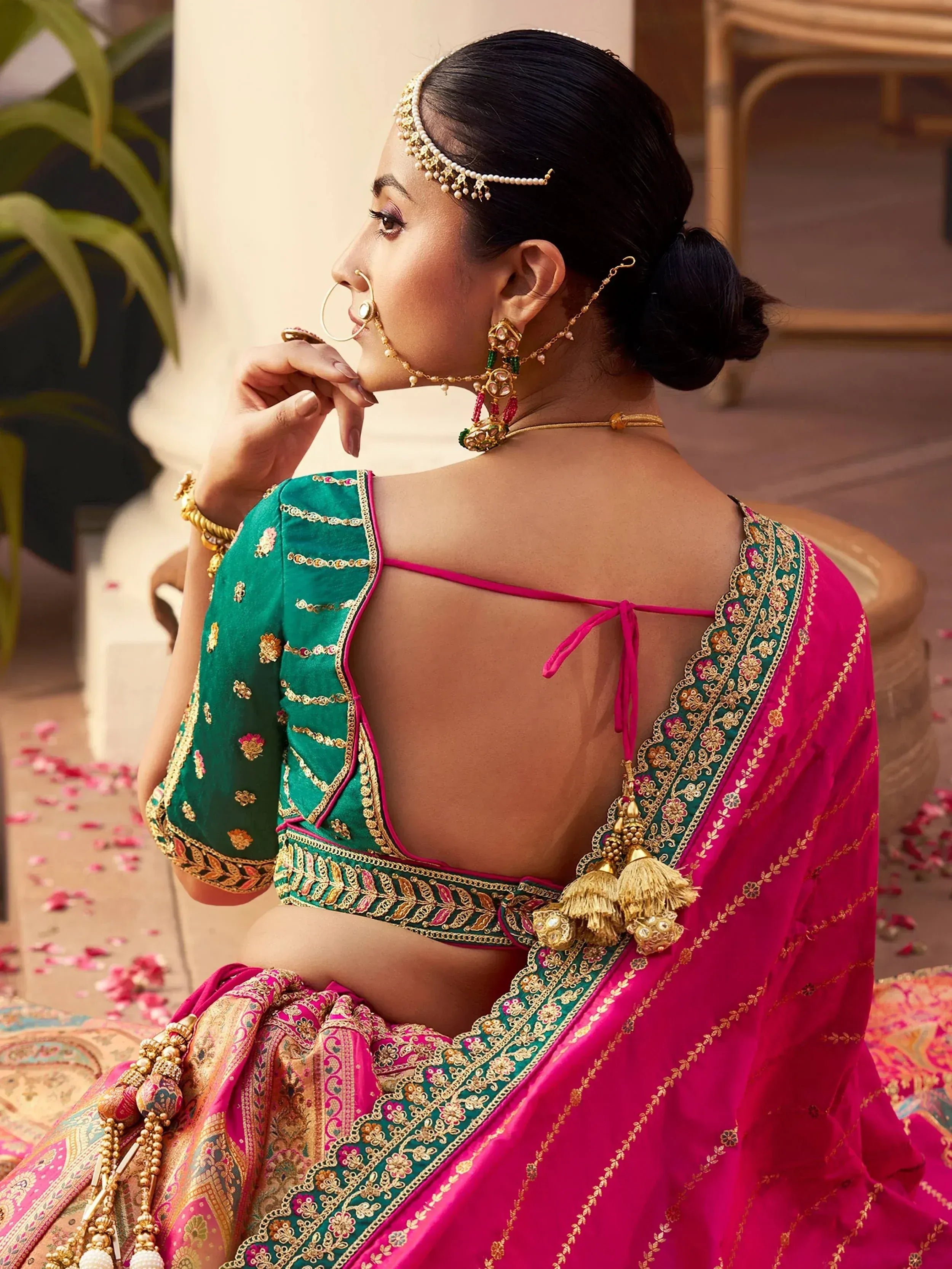 Elegant Indian bride in pink and green embroidered lehenga choli with gold jewelry and maang tikka